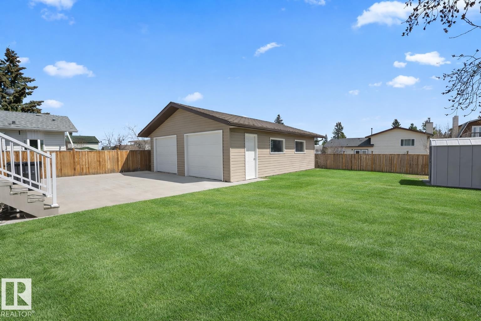 Expansive green lawn with a detached two-car garage featuring two white garage doors and a separate entry door - 1304 12 Street, Cold Lake, AB - Outdoor
