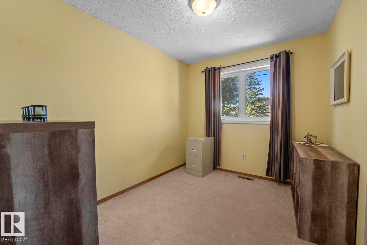 Carpeted interior space with a window featuring horizontal blinds and dark drapery, light yellow wall color, and a textured ceiling - 1304 12 Street, Cold Lake, AB - Indoor