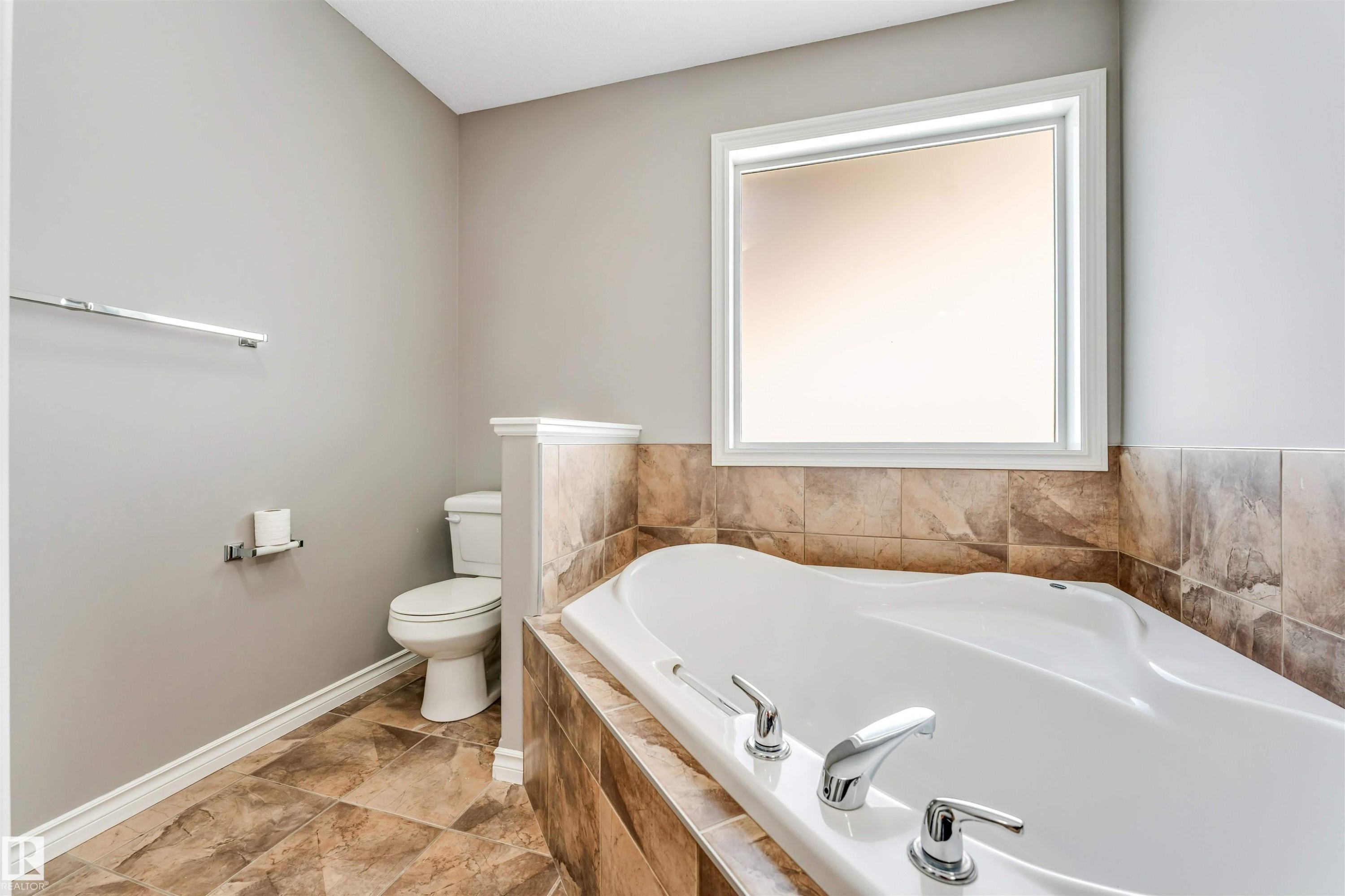 Soaking tub with chrome fixtures, surrounded by earth-toned tilework - 2138 32B Street, Edmonton, AB - Indoor Photo Showing Bathroom