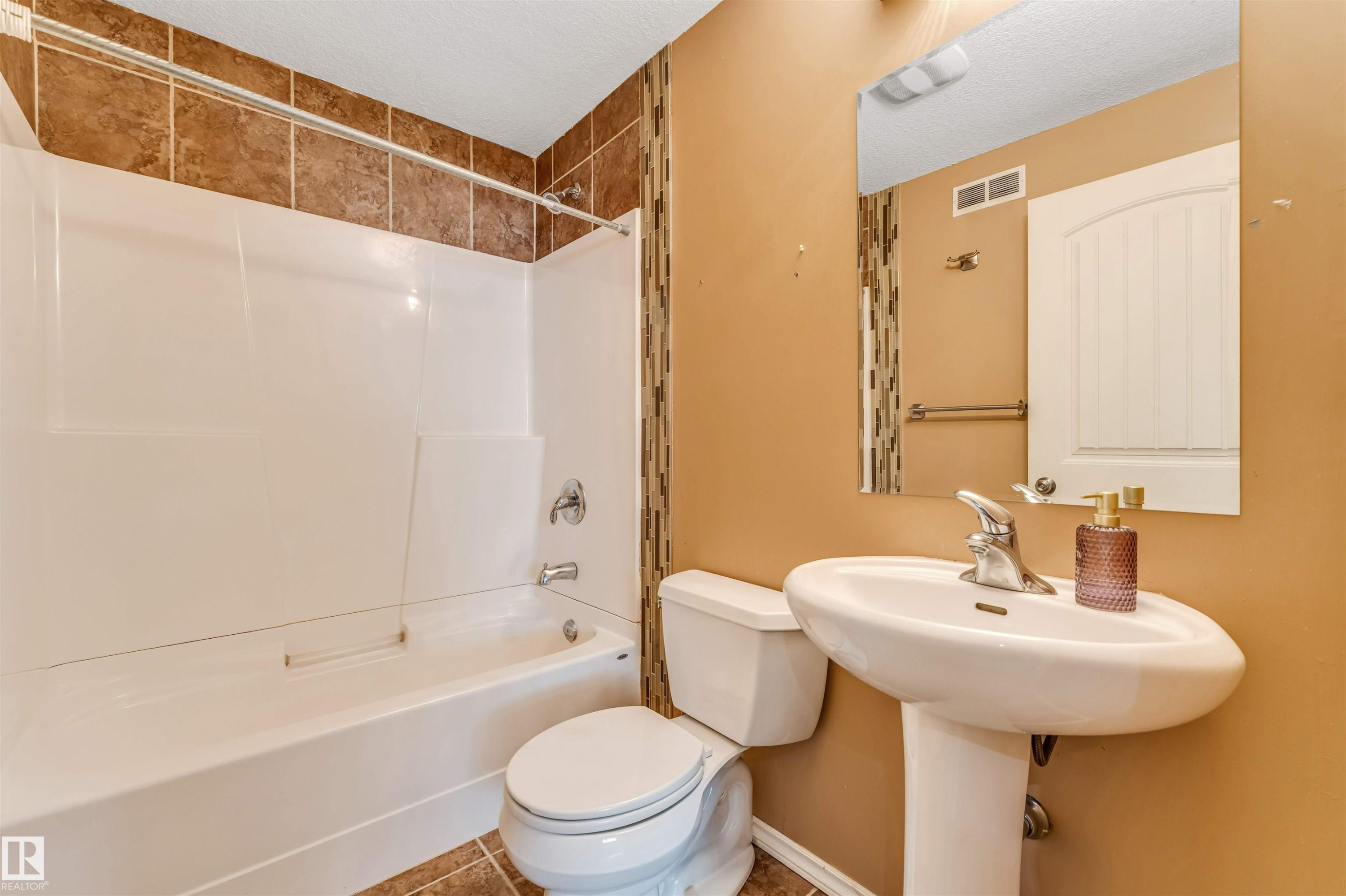 Bathroom featuring a pedestal sink with a chrome faucet, a white tub/shower combination, and complementary brown floor and shower wall tiles - 2138 32B Street, Edmonton, AB - Indoor Photo Showing Bathroom