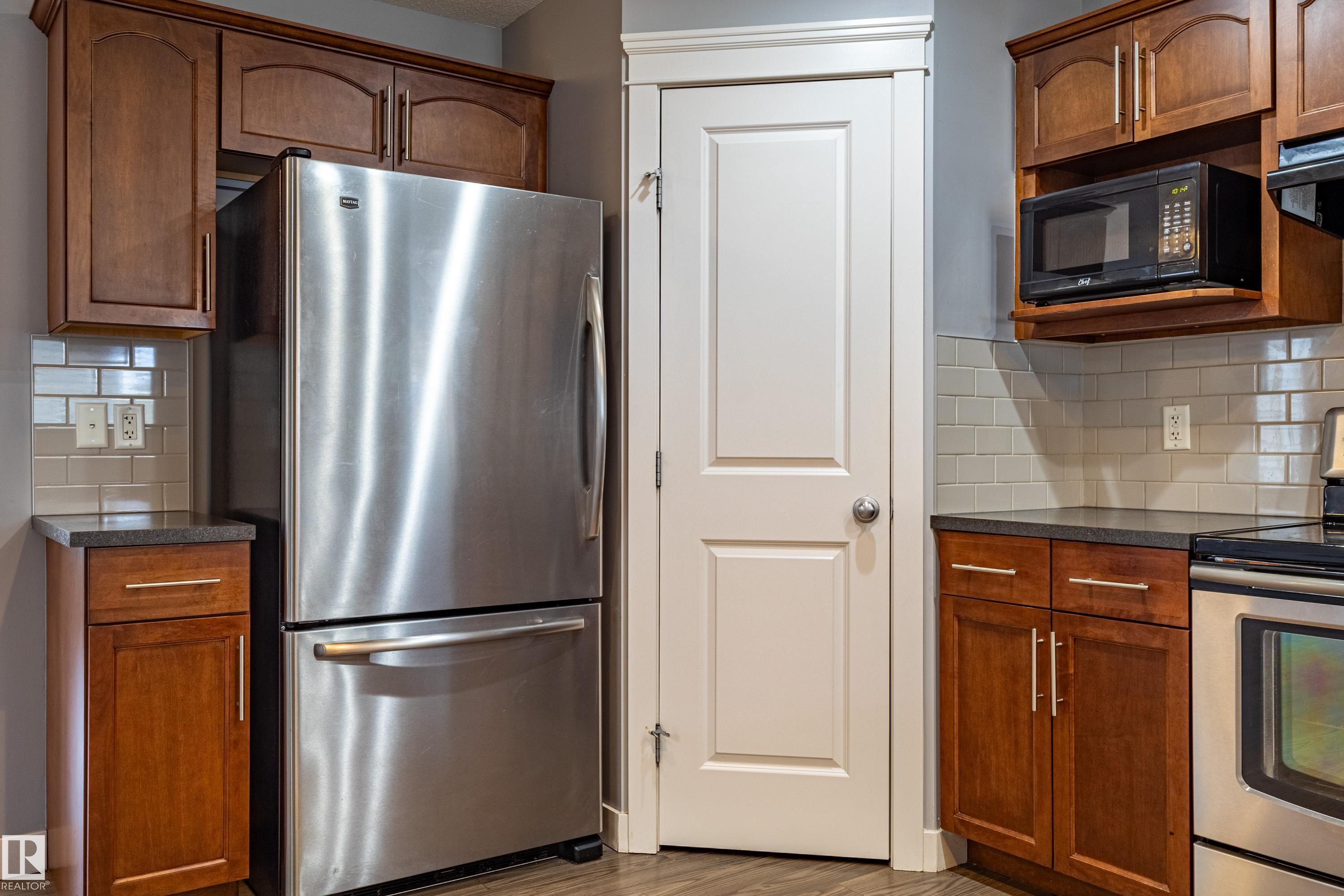 Kitchen featuring wood cabinetry, dark countertops, a stainless steel refrigerator, and a light-toned tile backsplash - 17715 6 Avenue, Edmonton, AB - Indoor Photo Showing Kitchen With Stainless Steel Kitchen