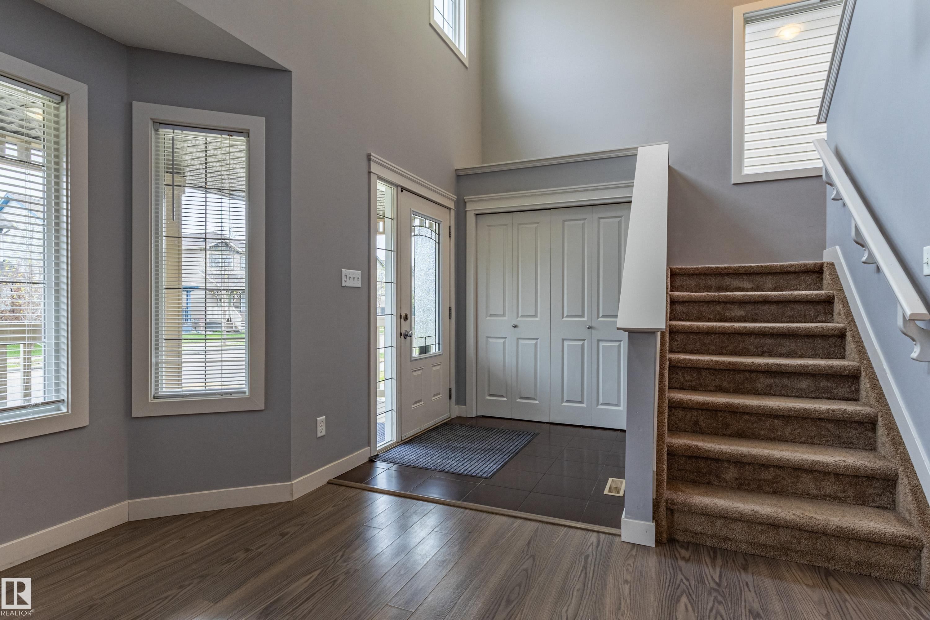 Entryway featuring wood-finish flooring, a carpeted staircase with white handrails, a front door with decorative glass inserts, and a coat closet with bi-fold doors - 17715 6 Avenue, Edmonton, AB - Indoor Photo Showing Other Room