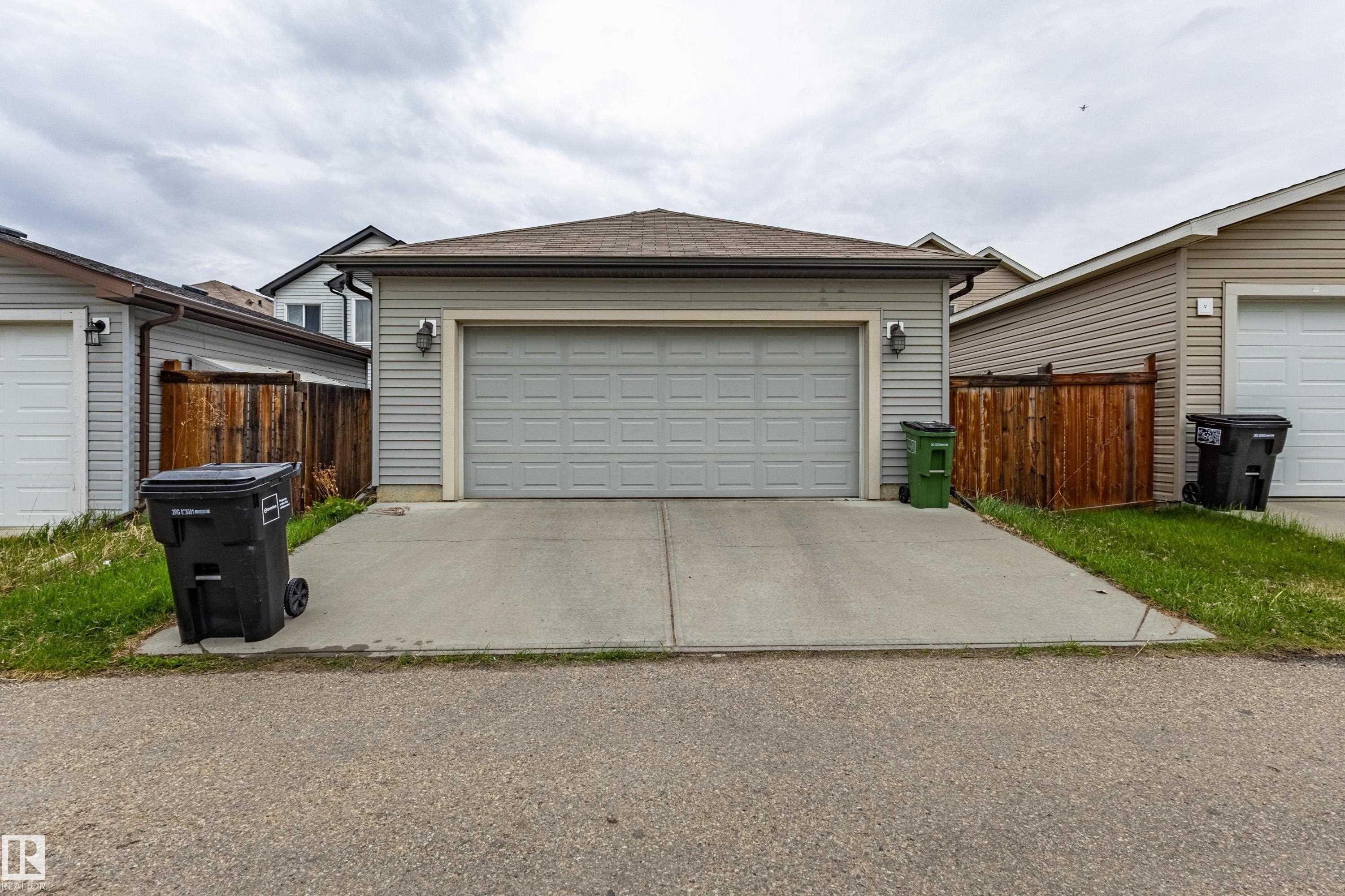Rear-facing attached garage with a panel-style door and twin exterior wall sconces - 17715 6 Avenue, Edmonton, AB - Outdoor With Exterior