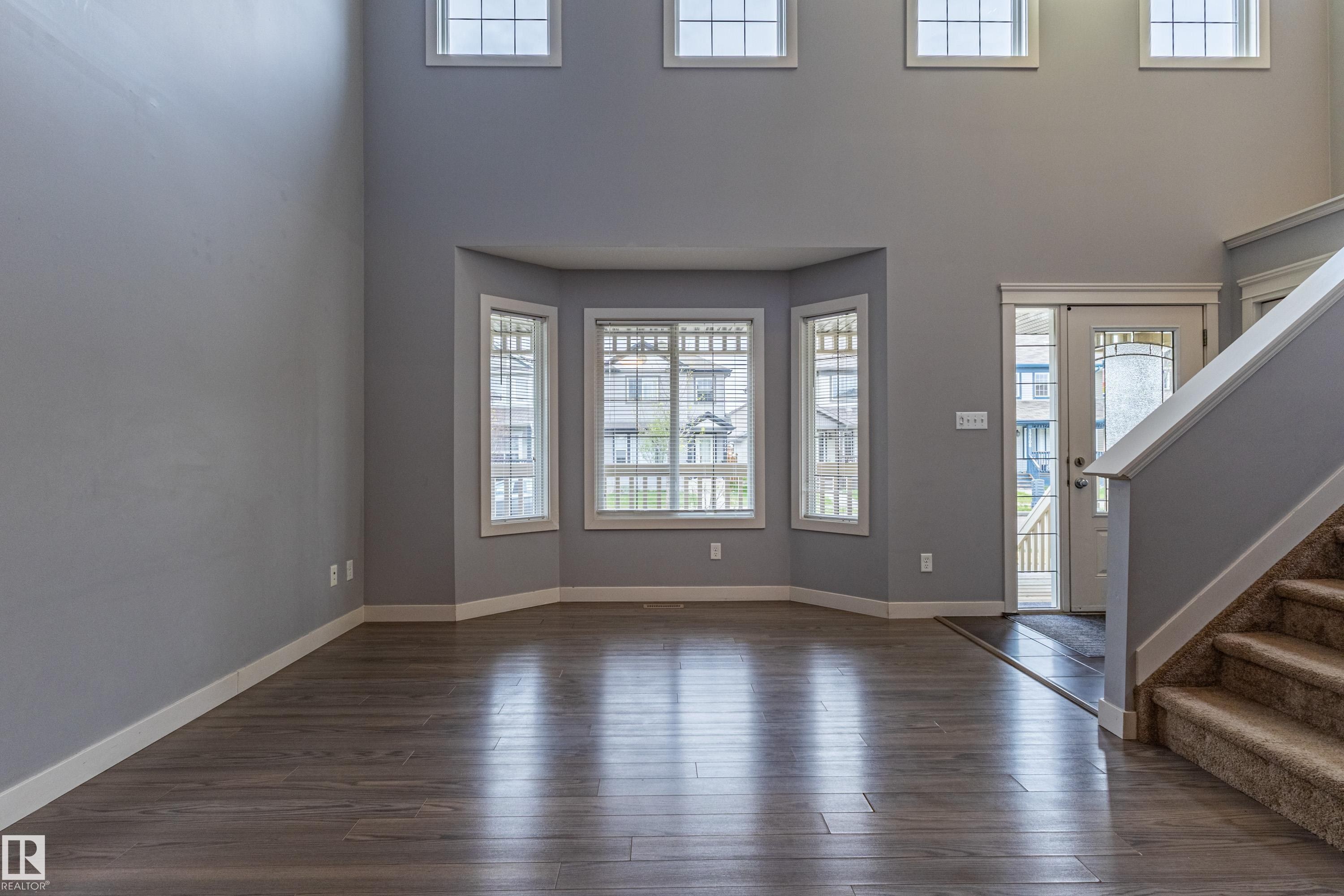 Two-story foyer featuring wood-finish flooring, a bay window with multiple panes, and a staircase with carpeted treads and a white balustrade - 17715 6 Avenue, Edmonton, AB - Indoor Photo Showing Other Room