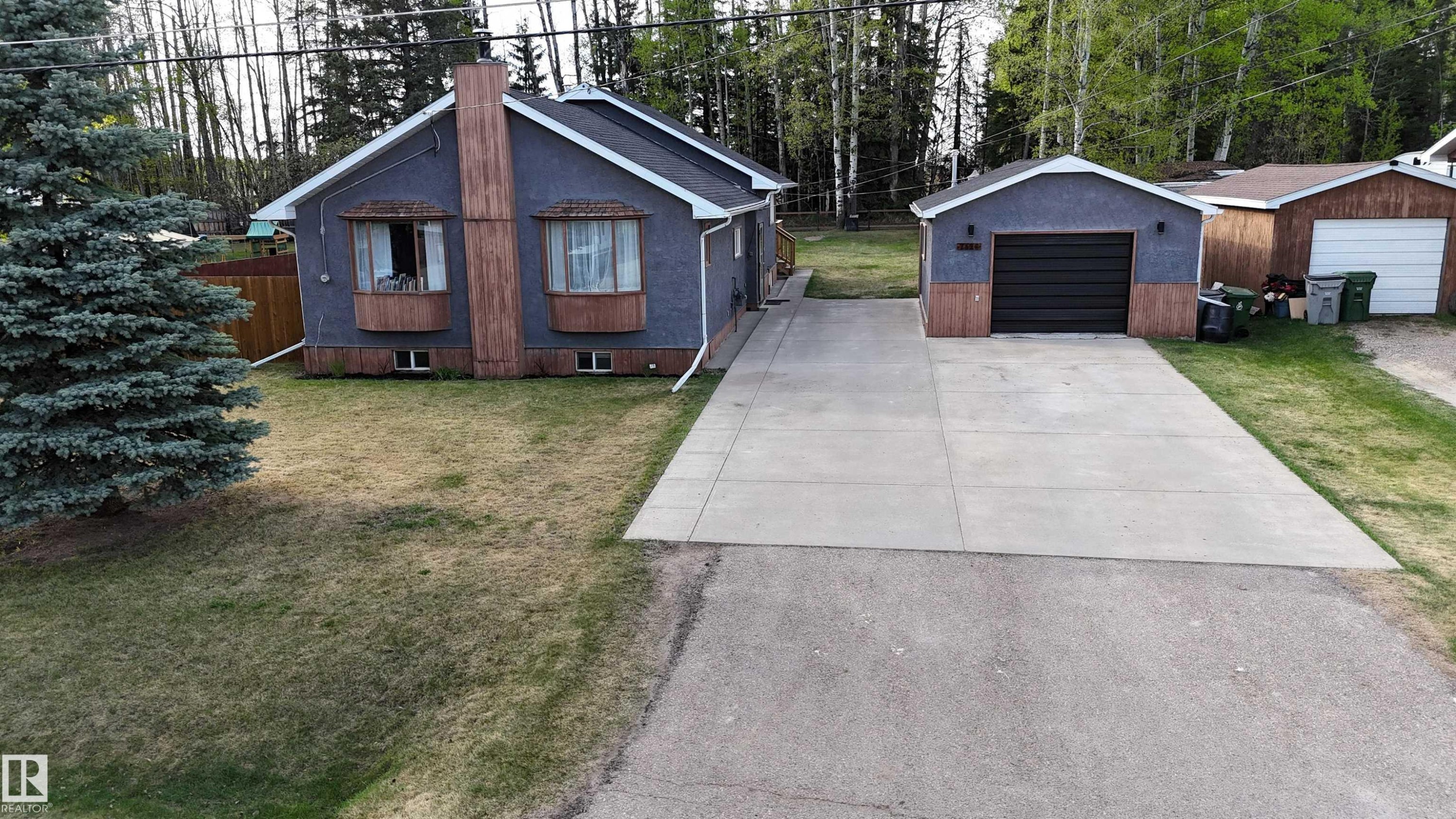 Exterior featuring gray siding, two prominent bay windows, and a detached single-car garage with a black door - 7126 4A Ave, Edson, AB - Outdoor