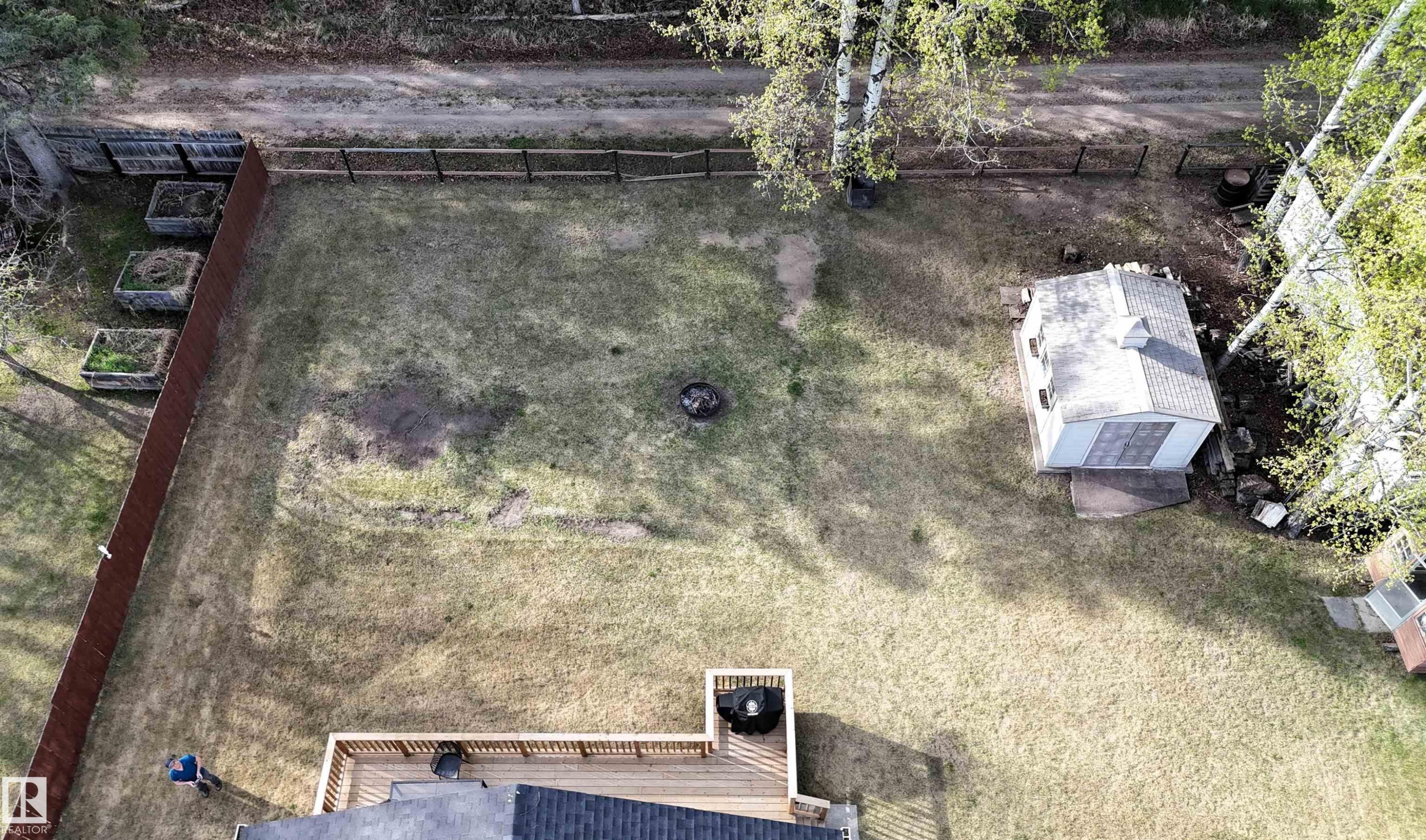 Expansive backyard featuring a wood deck, a storage shed, a fire pit area, and raised garden beds along the perimeter - 7126 4A Ave, Edson, AB - Outdoor With View
