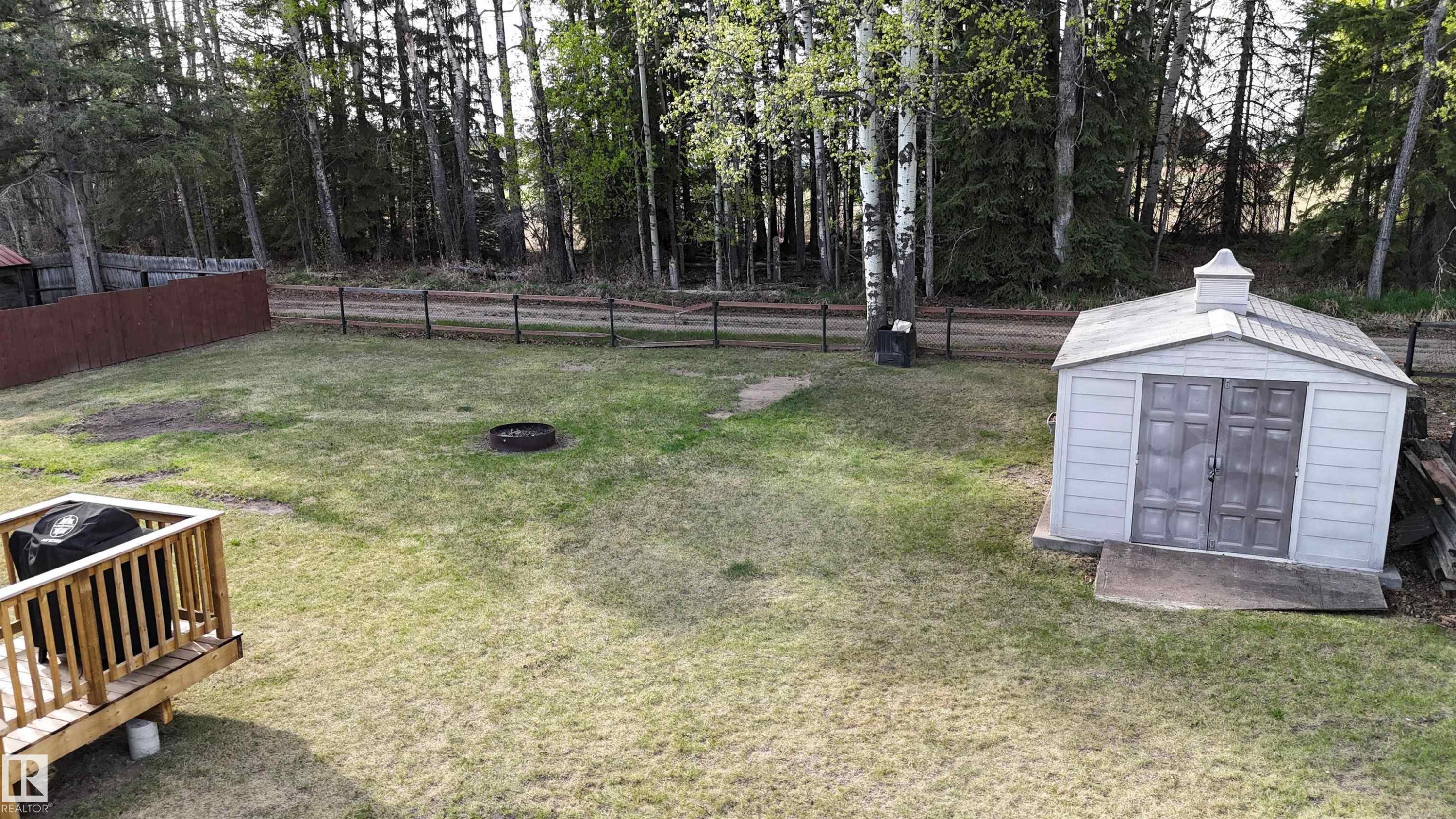 Expansive backyard featuring a wood deck, a white storage shed, a fire pit area, and a tree-lined perimeter - 7126 4A Ave, Edson, AB - Outdoor