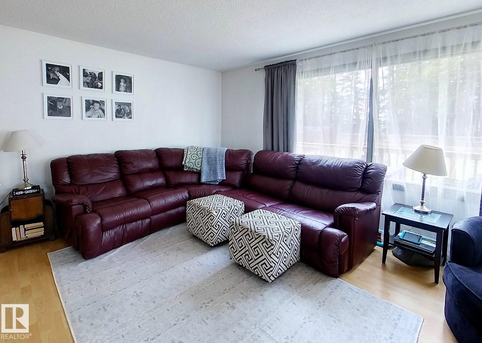 Living area featuring wood-finish flooring and expansive windows with sheer and blackout draperies - 7126 4A Ave, Edson, AB - Indoor Photo Showing Living Room