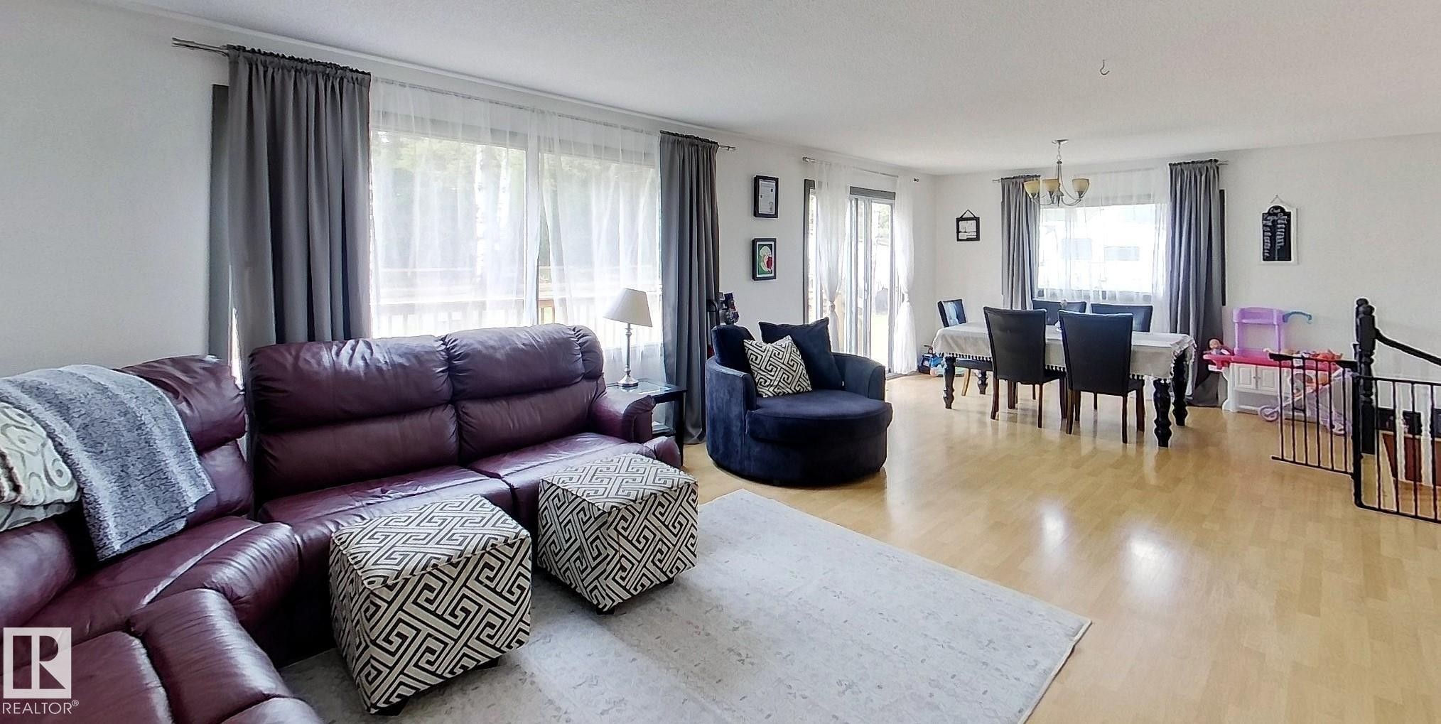 Open-concept living space featuring wood-finish flooring, white walls, and substantial windows with privacy sheers and drapery - 7126 4A Ave, Edson, AB - Indoor Photo Showing Living Room