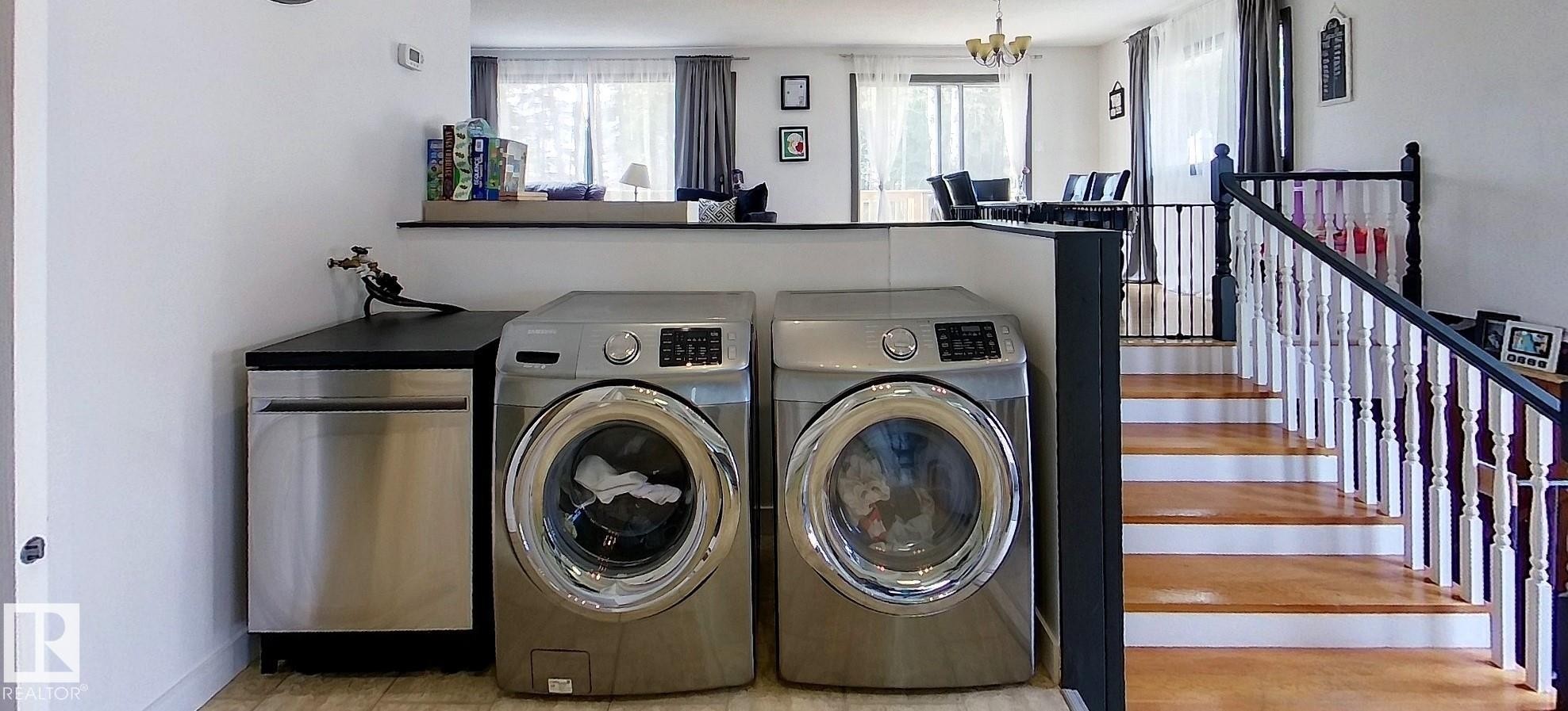 Integrated laundry area featuring stainless steel front-loading appliances and a built-in stainless steel dishwasher - 7126 4A Ave, Edson, AB - Indoor Photo Showing Laundry Room