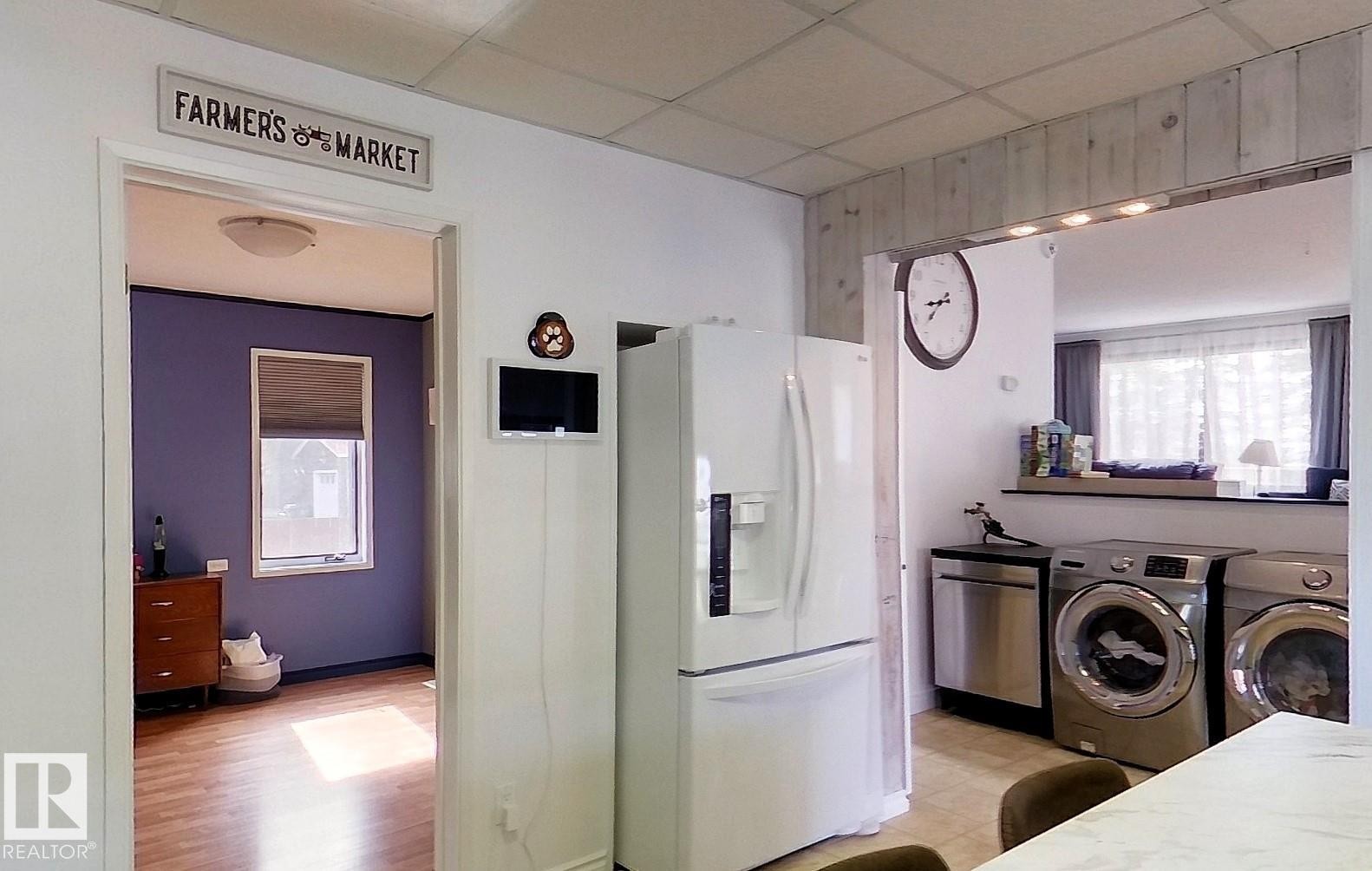 Kitchen area featuring a white refrigerator with water dispenser, stainless steel dishwasher, and front-loading washer and dryer units - 7126 4A Ave, Edson, AB - Indoor Photo Showing Laundry Room