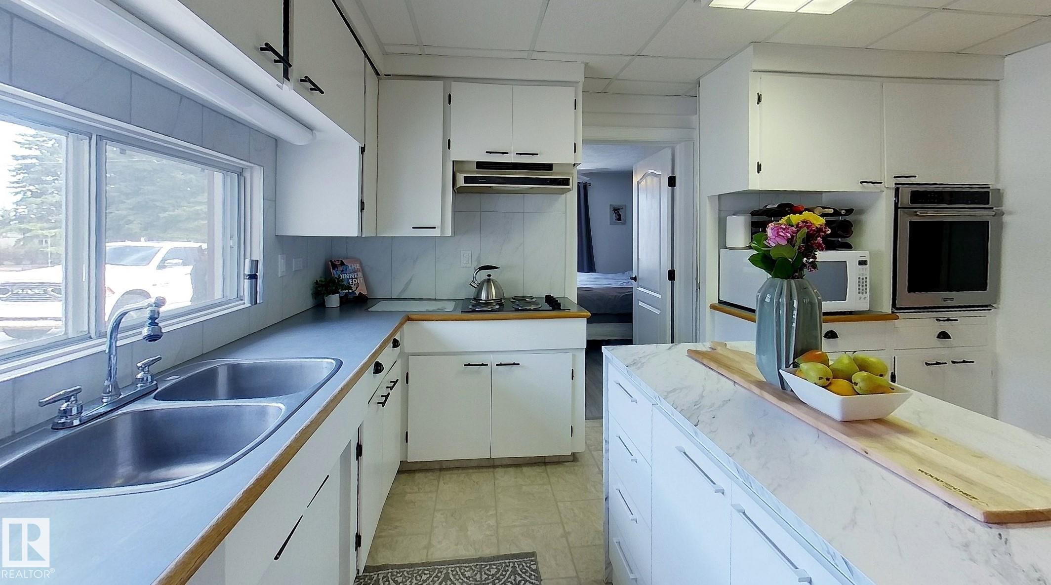 Bright kitchen featuring white cabinetry and a central island with a stone-finish countertop - 7126 4A Ave, Edson, AB - Indoor Photo Showing Kitchen With Double Sink
