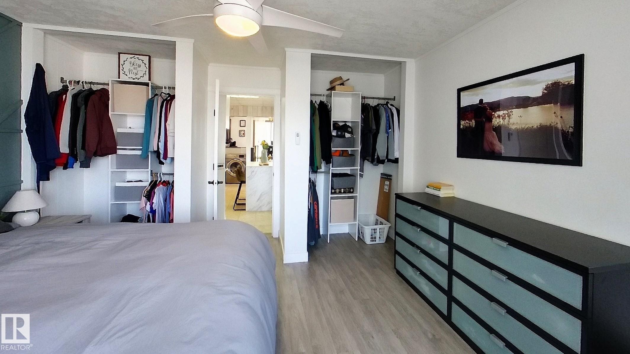 Bedroom space featuring light wood-finish flooring, a contemporary ceiling fan, and two open closets with built-in shelving and hanging rods - 7126 4A Ave, Edson, AB - Indoor Photo Showing Bedroom