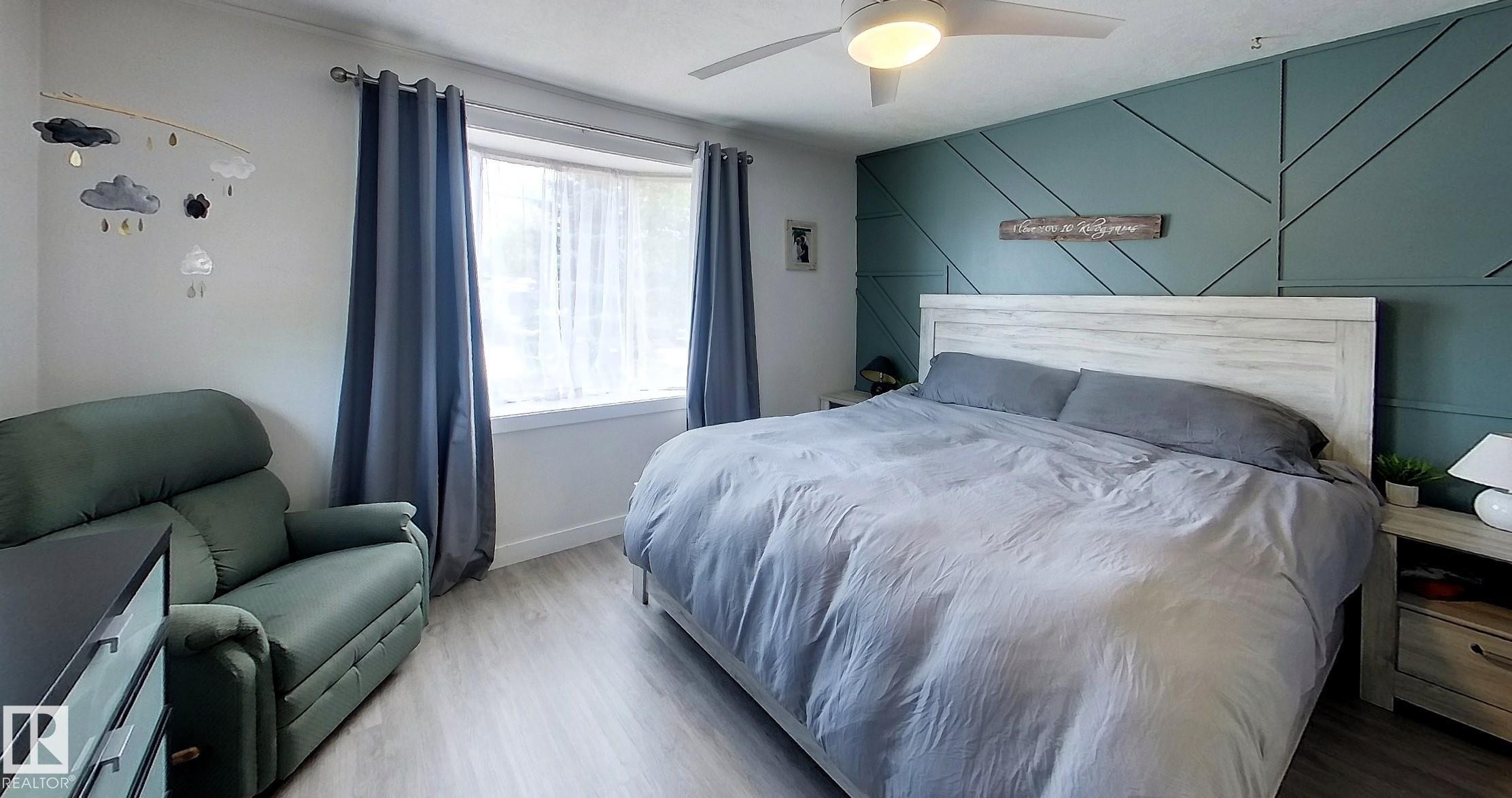 Bedroom featuring a decorative accent wall, wood-finish flooring, and a ceiling fan - 7126 4A Ave, Edson, AB - Indoor Photo Showing Bedroom