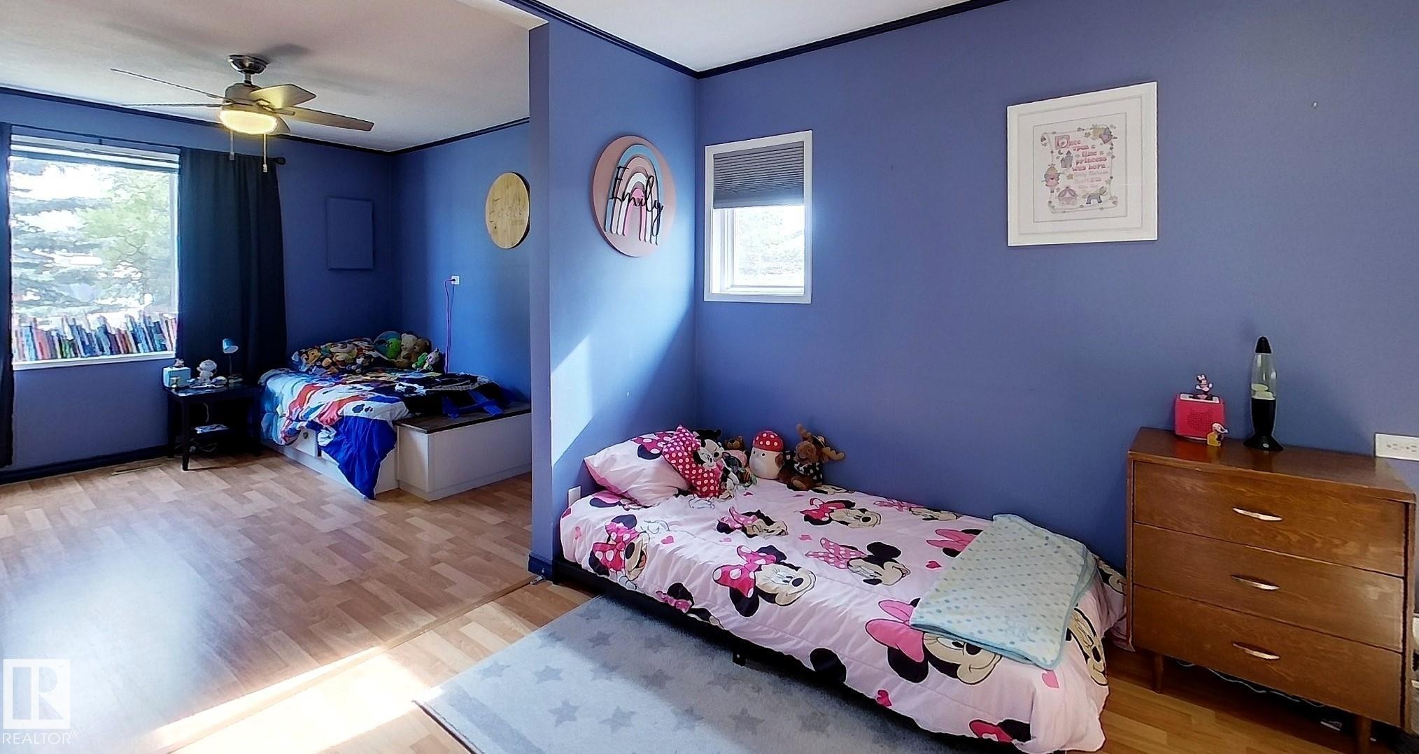 Spacious room featuring wood-finish flooring, multiple windows, and a ceiling fan with integrated lighting - 7126 4A Ave, Edson, AB - Indoor Photo Showing Bedroom