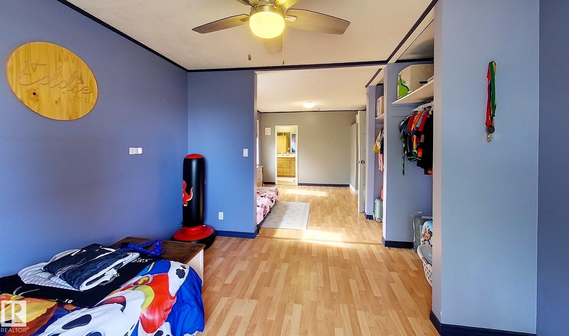 Interior space featuring wood-finish flooring, a ceiling fan with integrated lighting, and an open closet area with shelving - 7126 4A Ave, Edson, AB - Indoor