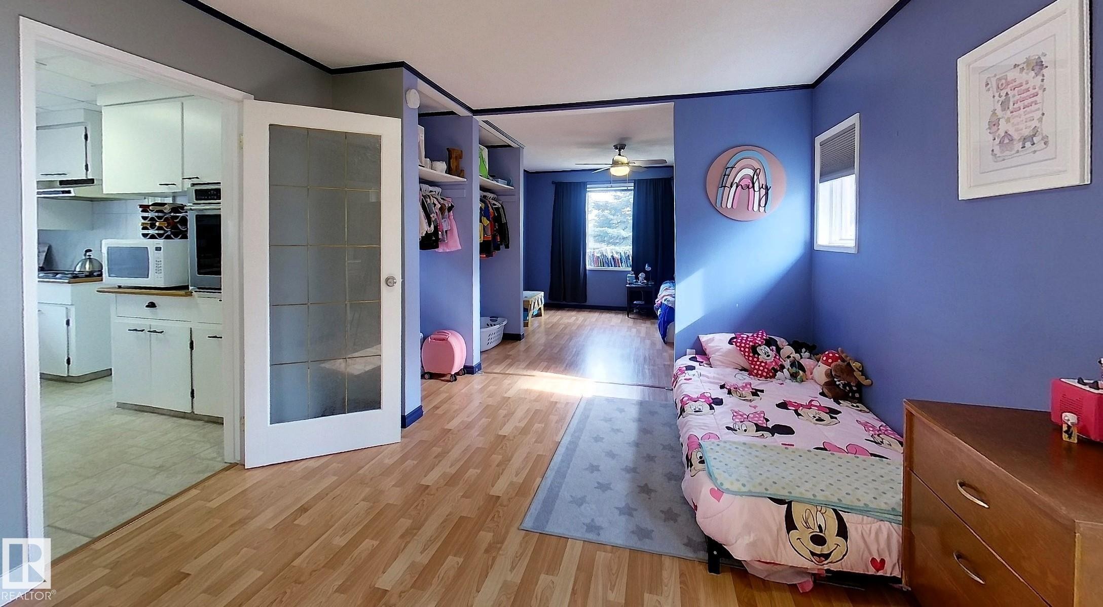 Open concept interior featuring wood-finish flooring and a pocket door with frosted glass panels - 7126 4A Ave, Edson, AB - Indoor Photo Showing Other Room