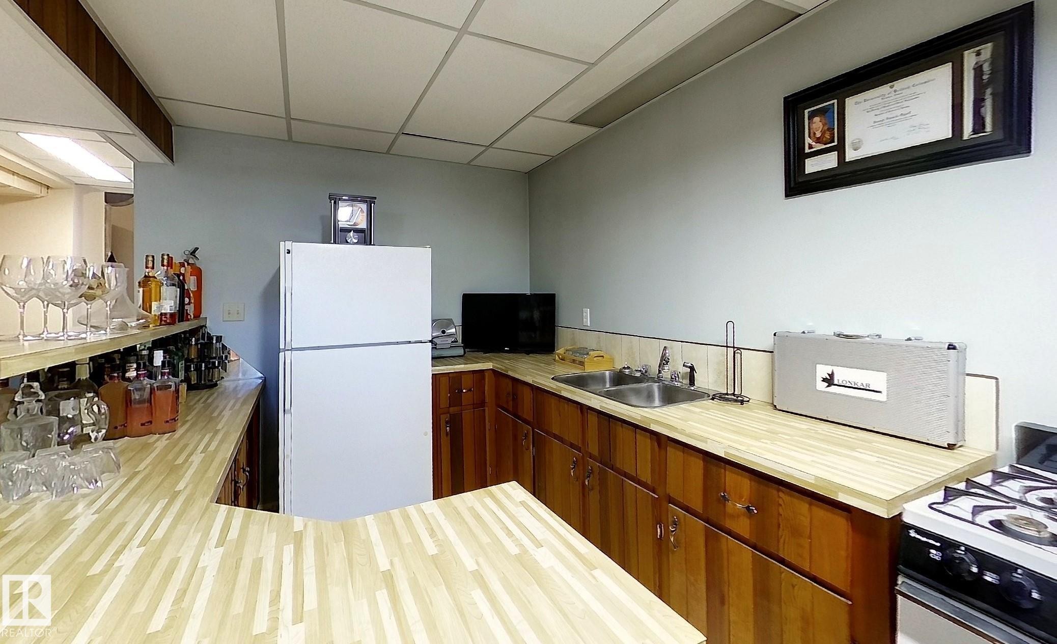 Kitchenette featuring a full-size refrigerator, corner sink, gas range, and wood-finish countertops - 7126 4A Ave, Edson, AB - Indoor Photo Showing Kitchen With Double Sink