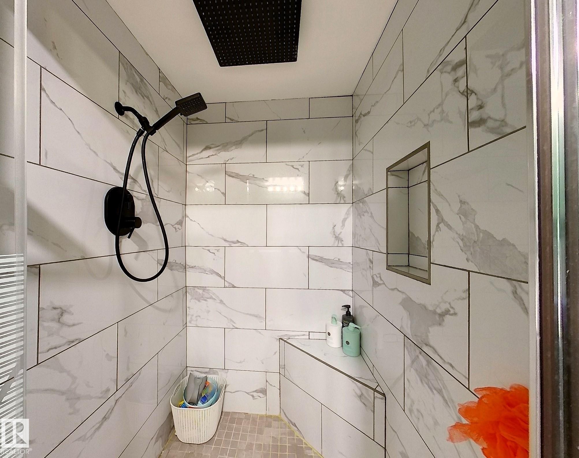 Tiled shower featuring a matte black rainfall showerhead and handheld sprayer, a built-in bench, and a recessed niche - 7126 4A Ave, Edson, AB - Indoor Photo Showing Bathroom