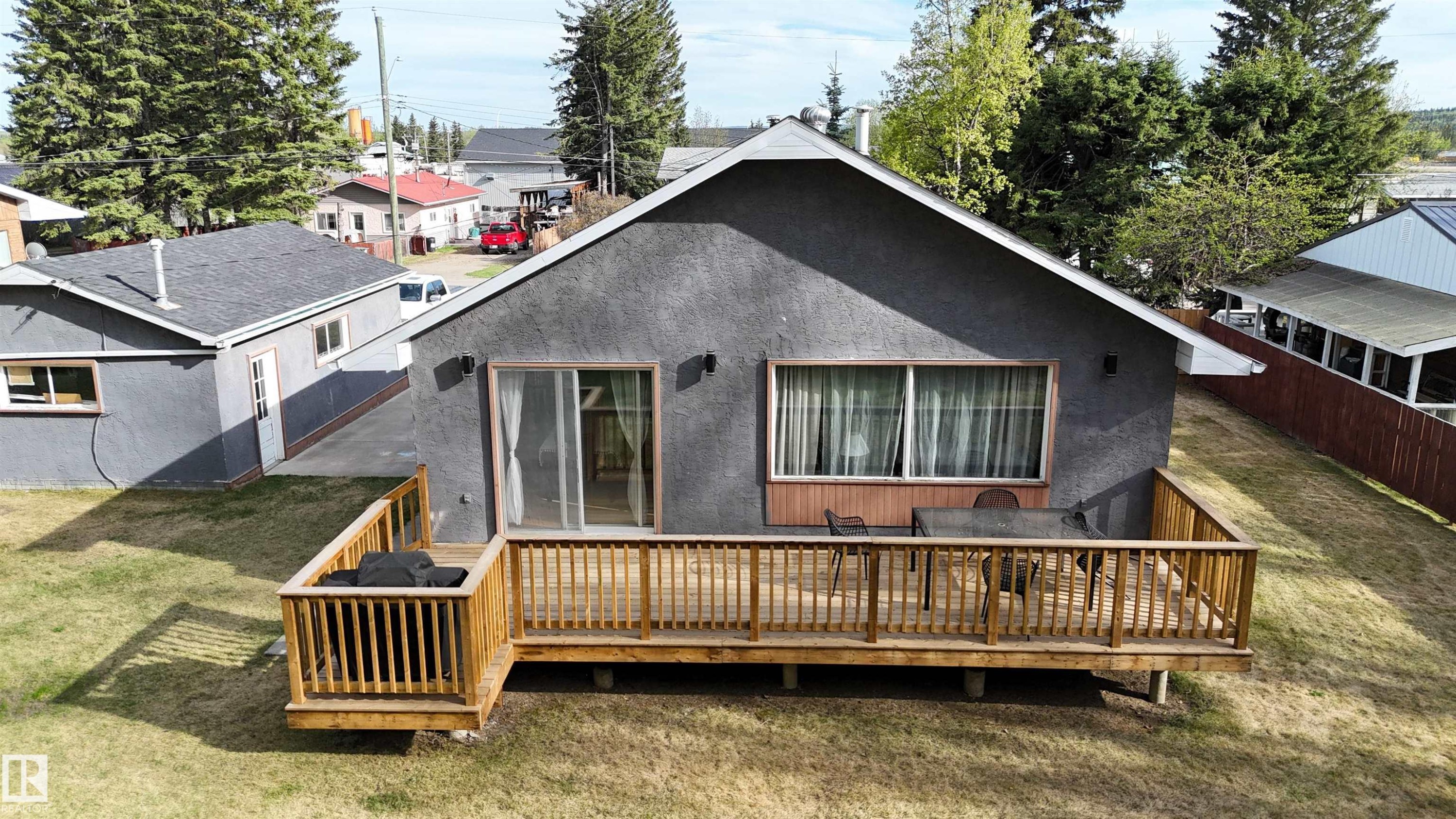 Gray stucco exterior featuring a wood deck with railings, sliding glass patio door, and a horizontal window with a wood trim - 7126 4A Ave, Edson, AB - Outdoor With Deck Patio Veranda