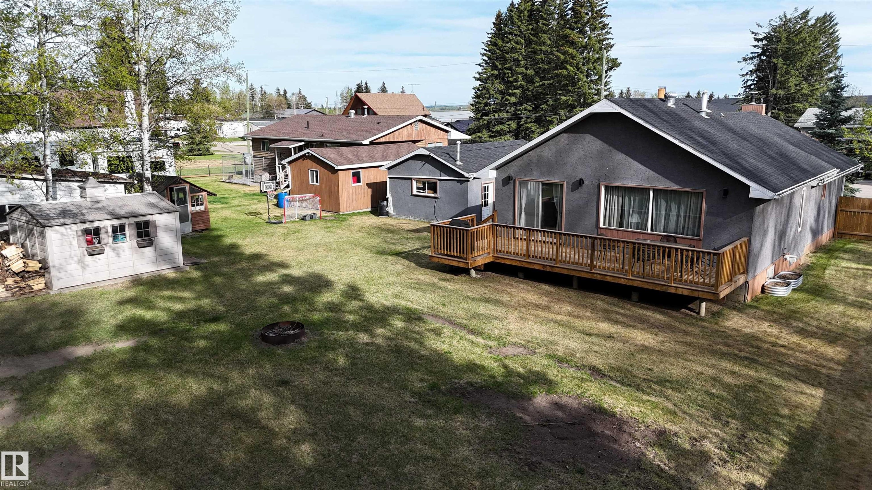 Rear exterior featuring a full-width wood deck, sliding glass door access, an additional shed, and a privacy fence - 7126 4A Ave, Edson, AB - Outdoor With Deck Patio Veranda
