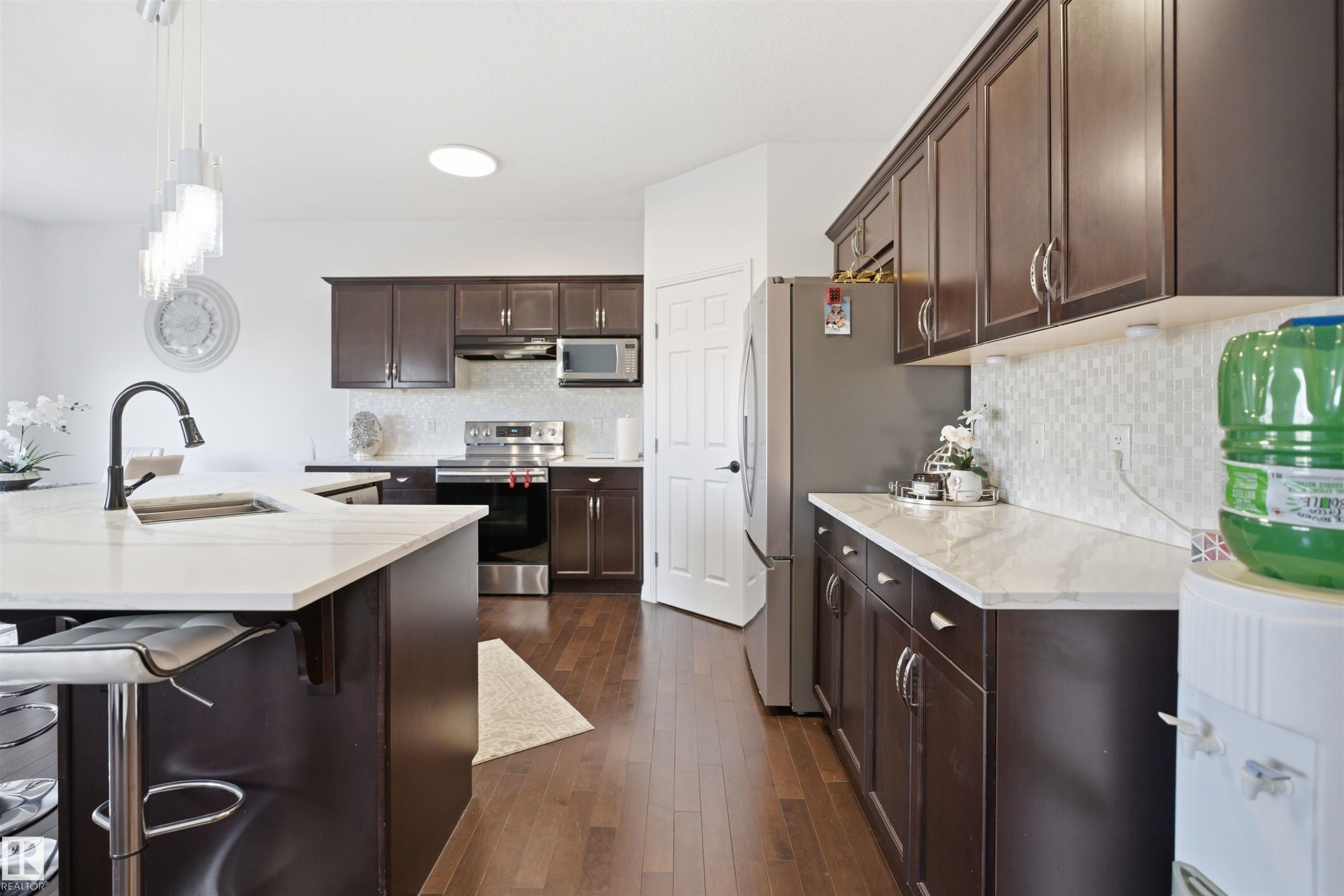 Kitchen featuring rich wood-finish cabinetry, light-toned countertops, and a white mosaic tile backsplash - 1453 Hays Way Nw, Edmonton, AB - Indoor Photo Showing Kitchen With Double Sink With Upgraded Kitchen
