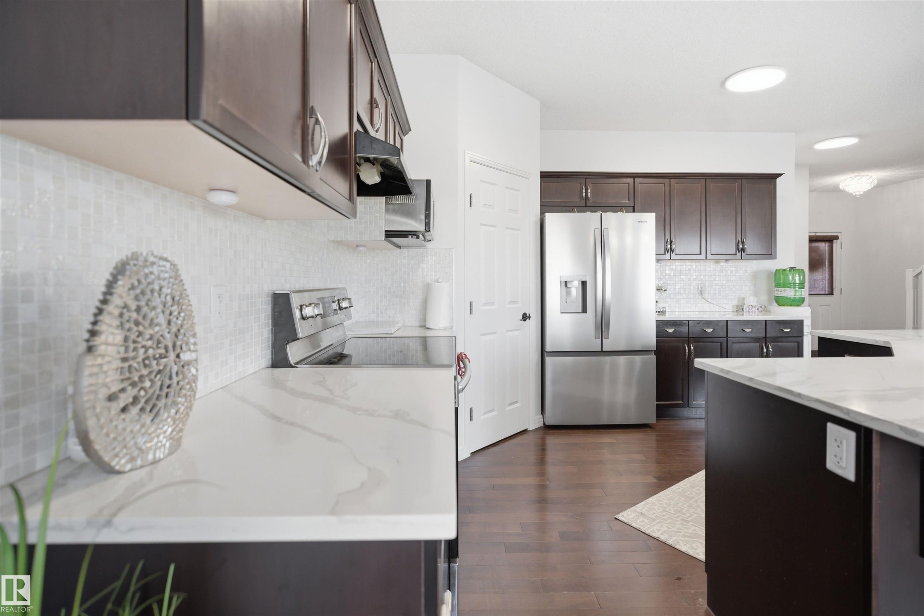 Kitchen featuring dark wood-finish cabinetry, stainless steel appliances, white patterned tile backsplash, and light-toned countertops with veining - 1453 Hays Way Nw, Edmonton, AB - Indoor Photo Showing Kitchen With Stainless Steel Kitchen With Upgraded Kitchen