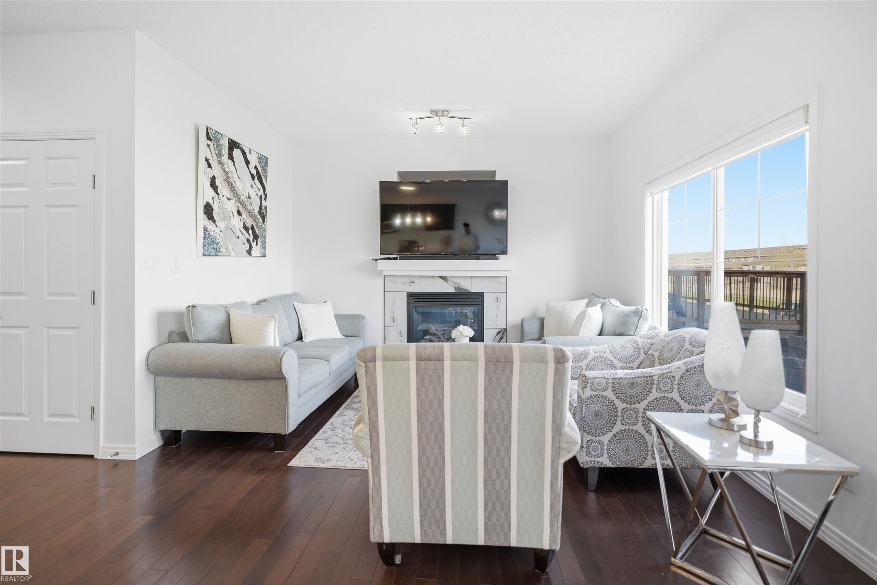 Living area featuring rich wood-finish flooring and a white marble-look fireplace with an electric insert - 1453 Hays Way Nw, Edmonton, AB - Indoor Photo Showing Living Room With Fireplace
