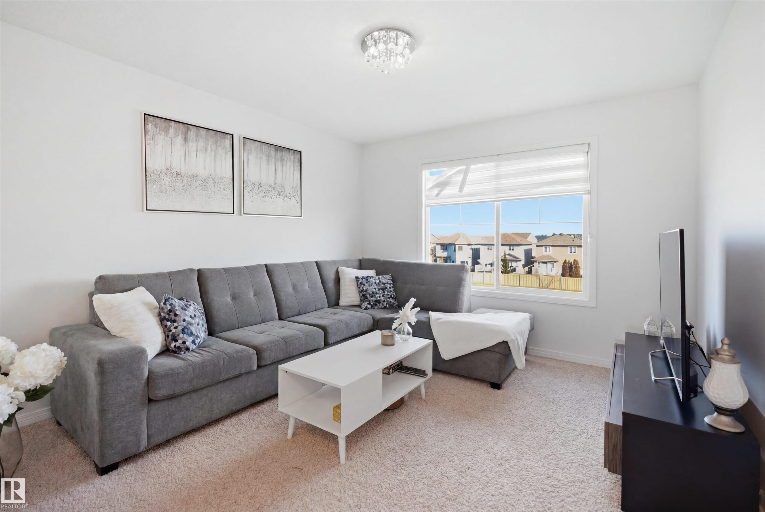Carpeted living area featuring a large picture window, white walls, and a contemporary ceiling light fixture - 1453 Hays Way Nw, Edmonton, AB - Indoor Photo Showing Living Room