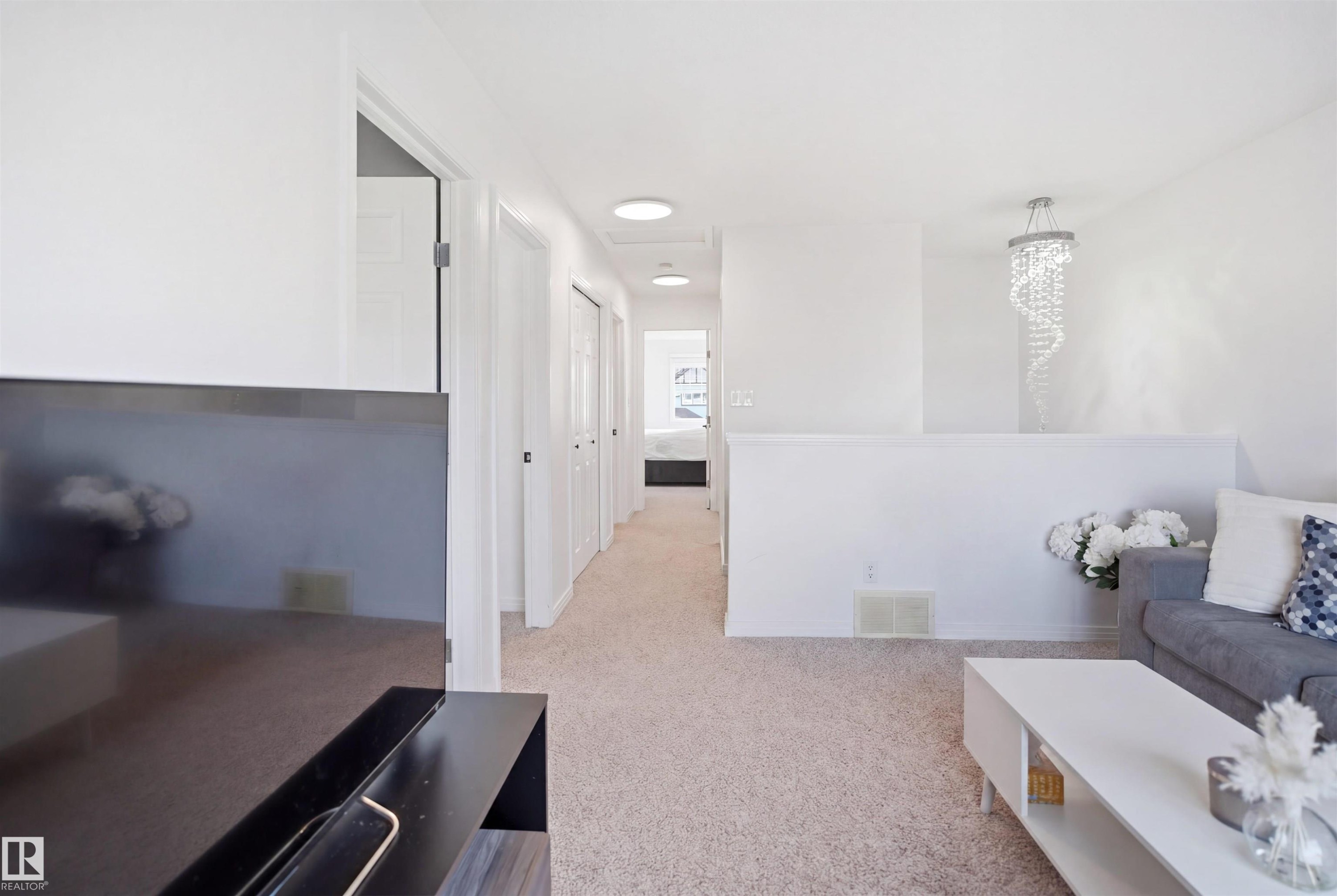 Carpeted open area featuring a contemporary chandelier and a half-wall partition - 1453 Hays Way Nw, Edmonton, AB - Indoor