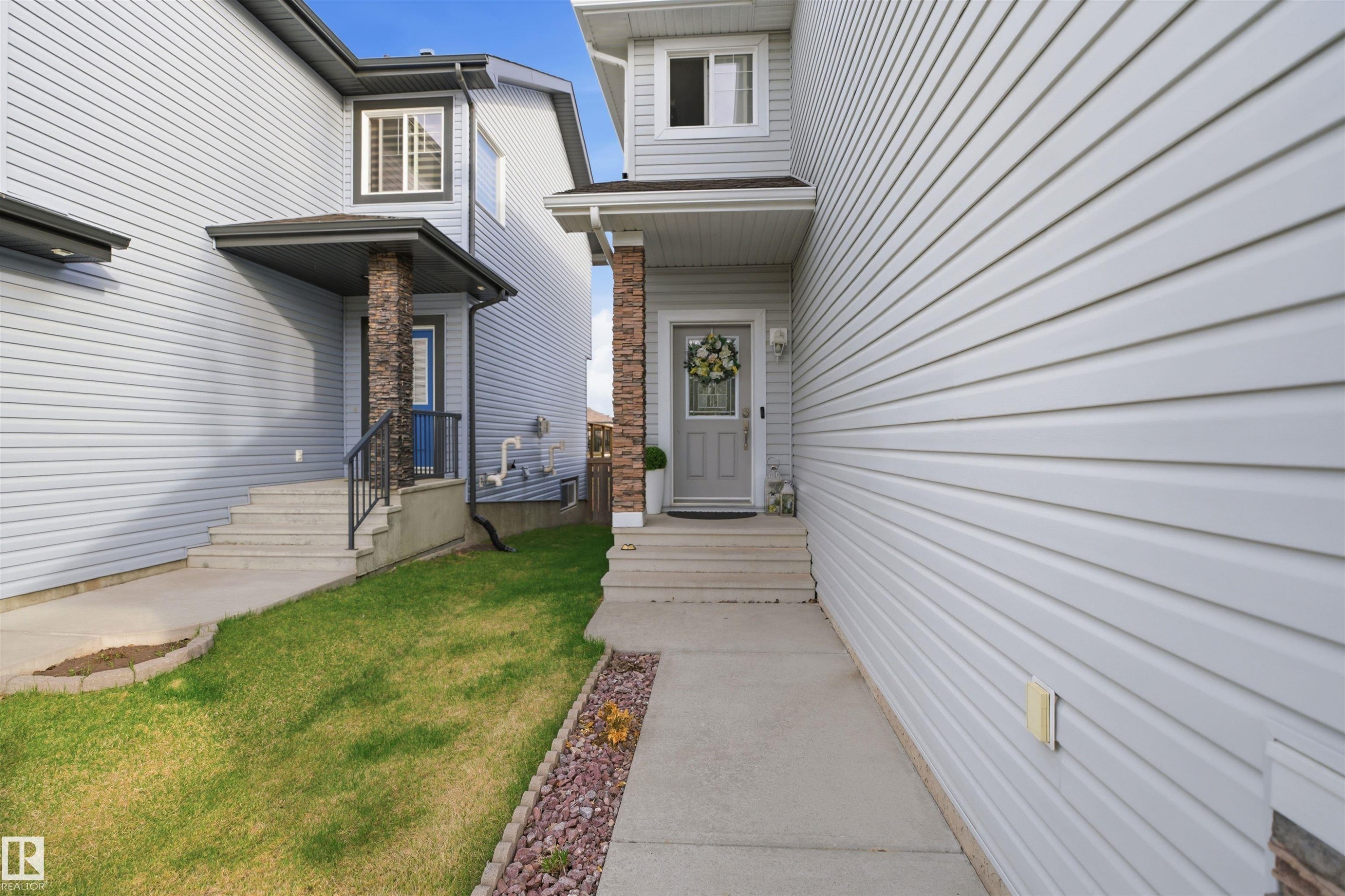 Entryway featuring a covered porch with a stone-clad pillar, concrete steps, and a gray front door with a window insert - 1453 Hays Way Nw, Edmonton, AB - Outdoor