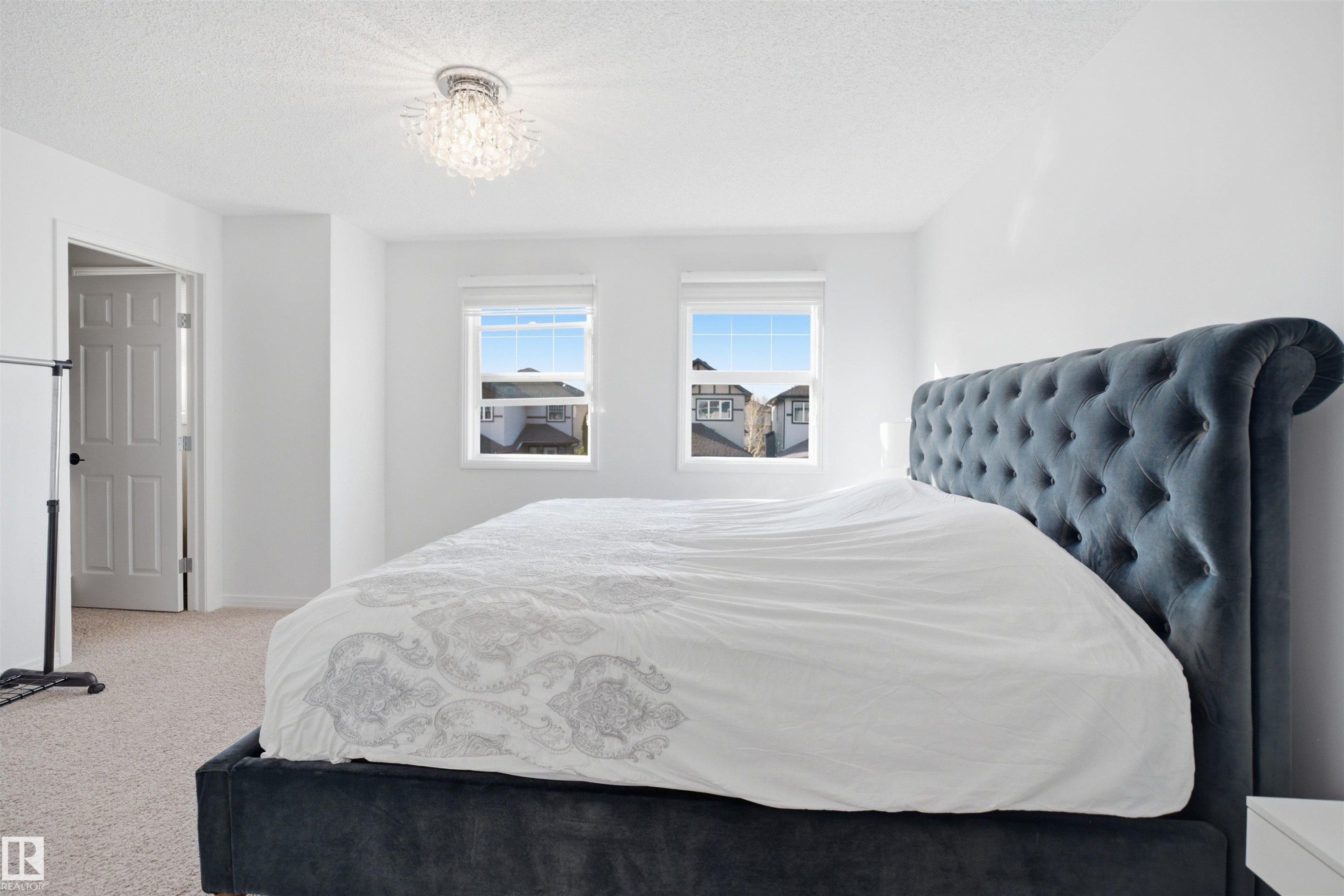 Bright room featuring dual windows, neutral-toned carpeting, white walls, a white paneled door, and a crystal flush mount ceiling light fixture - 1453 Hays Way Nw, Edmonton, AB - Indoor Photo Showing Bedroom