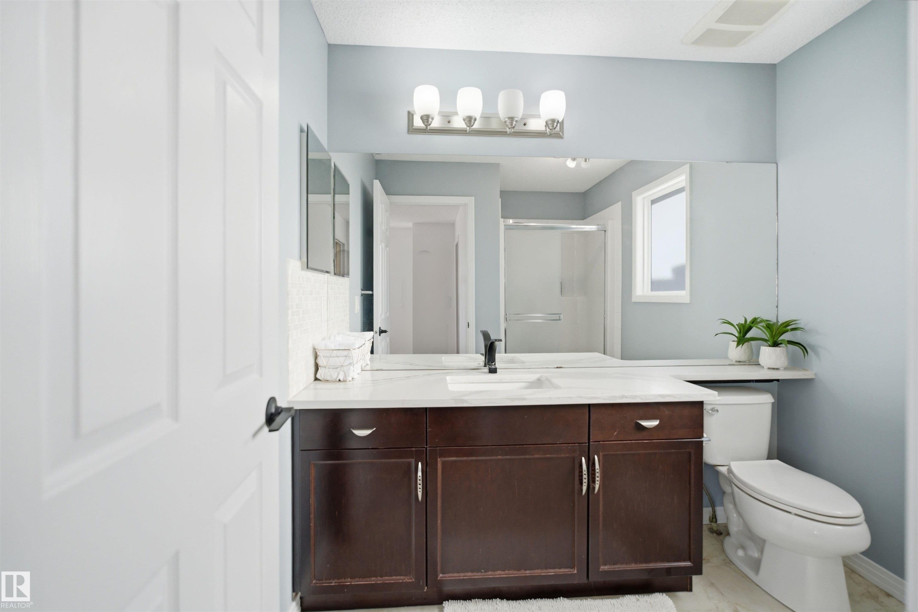 Bathroom featuring a dark wood-finish vanity with a white countertop and undermount sink, a large wall-mounted mirror, and a white toilet - 1453 Hays Way Nw, Edmonton, AB - Indoor Photo Showing Bathroom