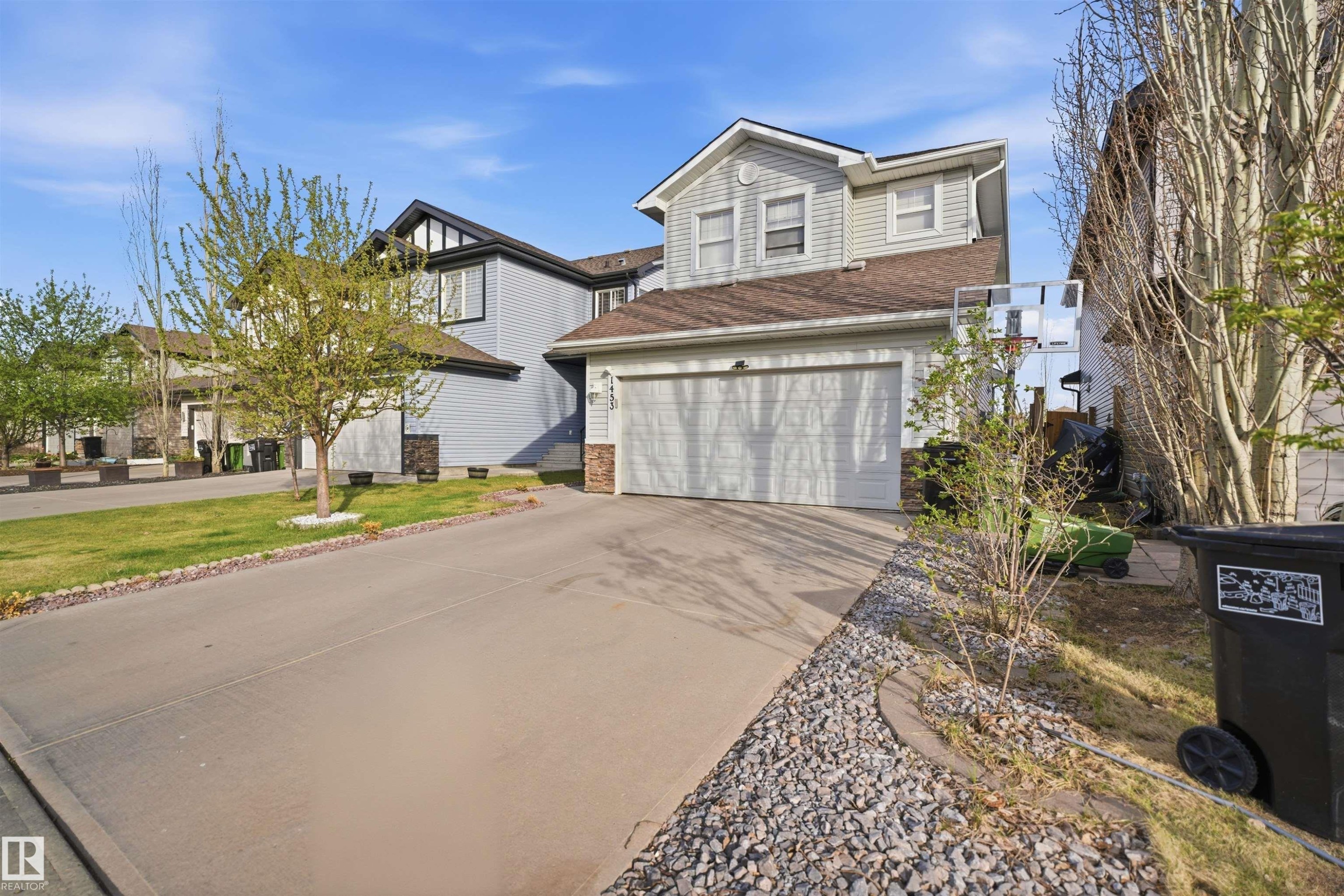 Two-story residence featuring light gray siding, an attached garage with a white door, a sloped brown roof, and a paved driveway - 1453 Hays Way Nw, Edmonton, AB - Outdoor