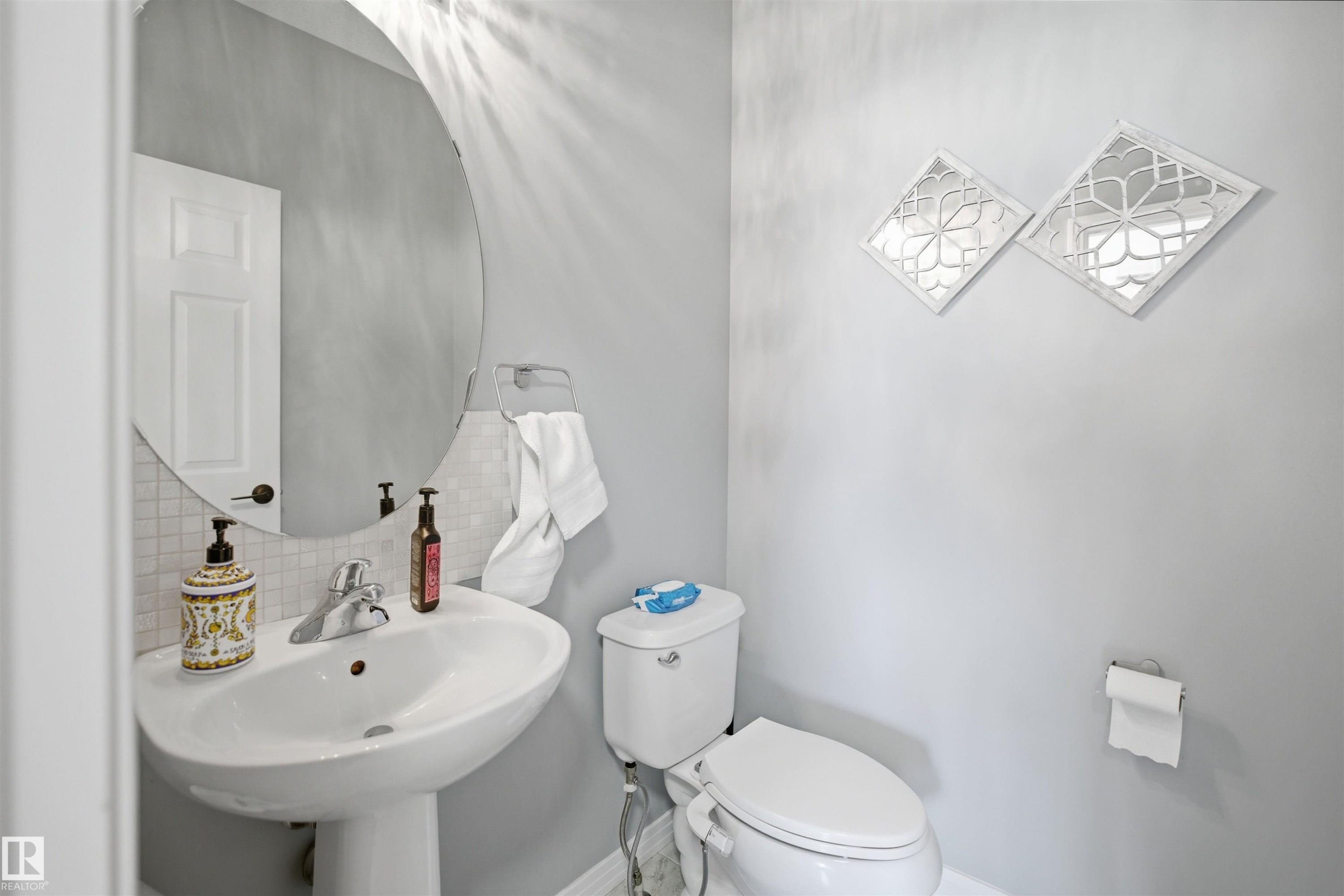 Pedestal sink with chrome faucet, circular mirror, and tile backsplash - 1453 Hays Way Nw, Edmonton, AB - Indoor Photo Showing Bathroom