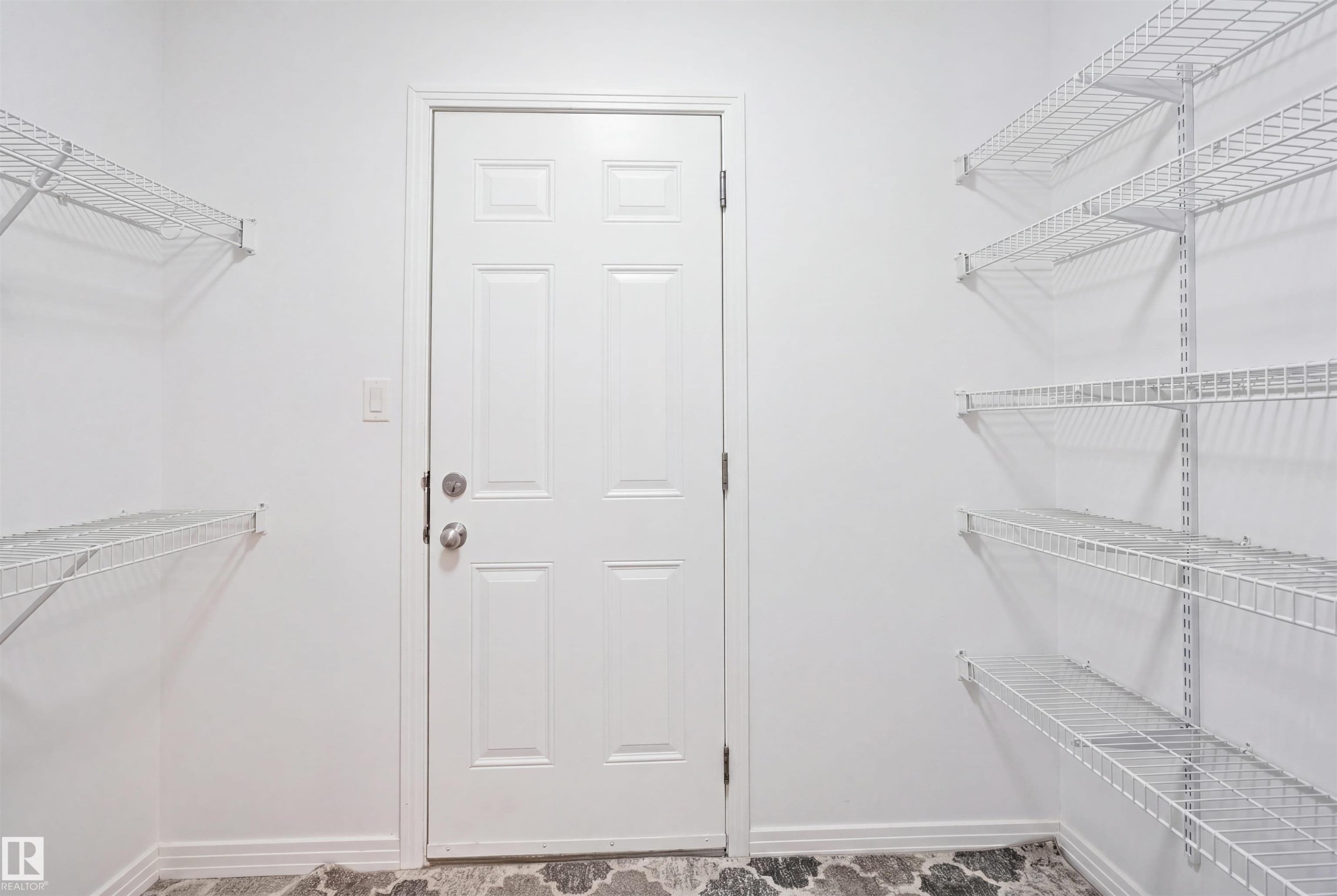 Utility room featuring a white paneled door, ample wall-mounted wire shelving, light-colored walls, and patterned flooring - 1453 Hays Way Nw, Edmonton, AB - Indoor With Storage