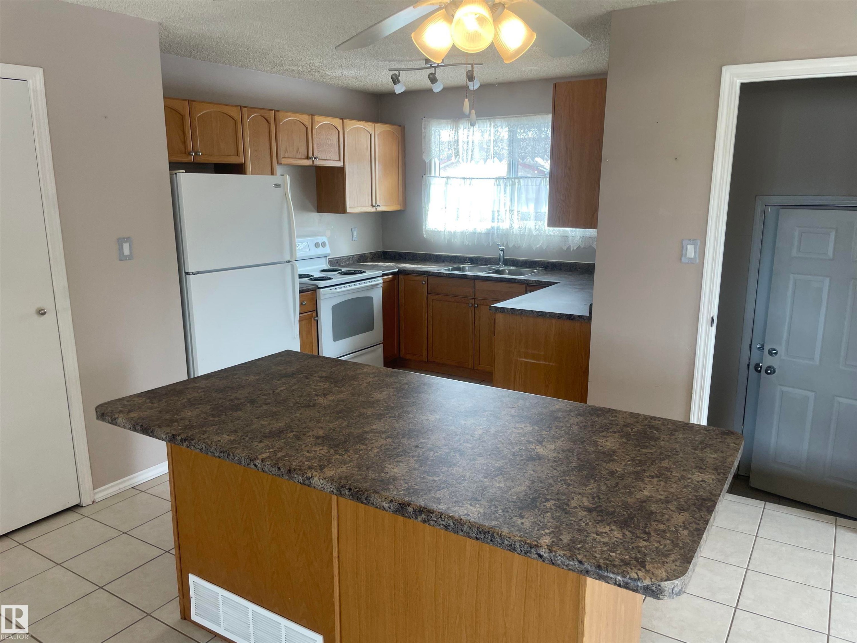 Kitchen featuring an island with a patterned countertop, light wood cabinetry, white appliances, and tiled flooring - 2629 129A Avenue, Edmonton, AB - Indoor Photo Showing Kitchen