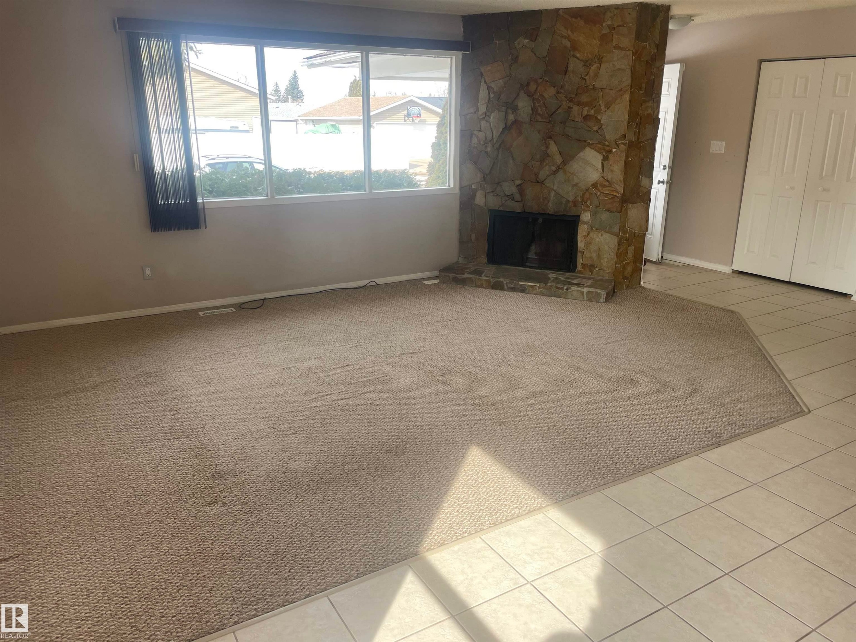 The living area features a stone fireplace, large windows providing natural light, and a combination of carpet and tiled flooring - 2629 129A Avenue, Edmonton, AB - Indoor With Fireplace