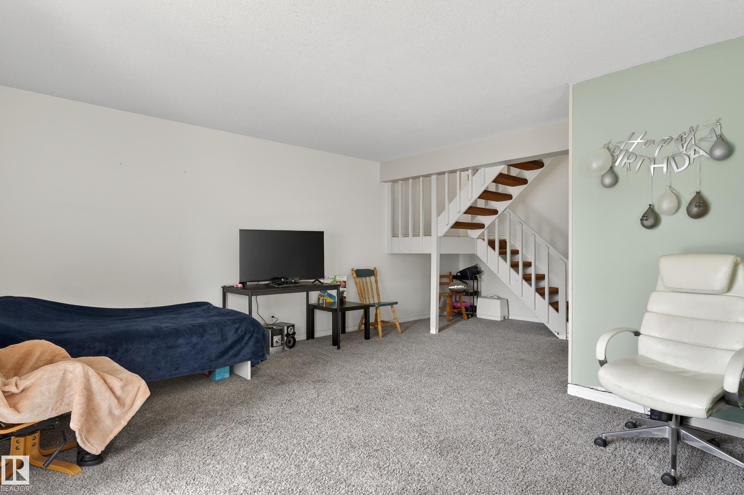 Open concept living area featuring a prominent staircase with wood-finish treads and white risers - 26E Meadowlark Village, Edmonton, AB - Indoor Photo Showing Other Room