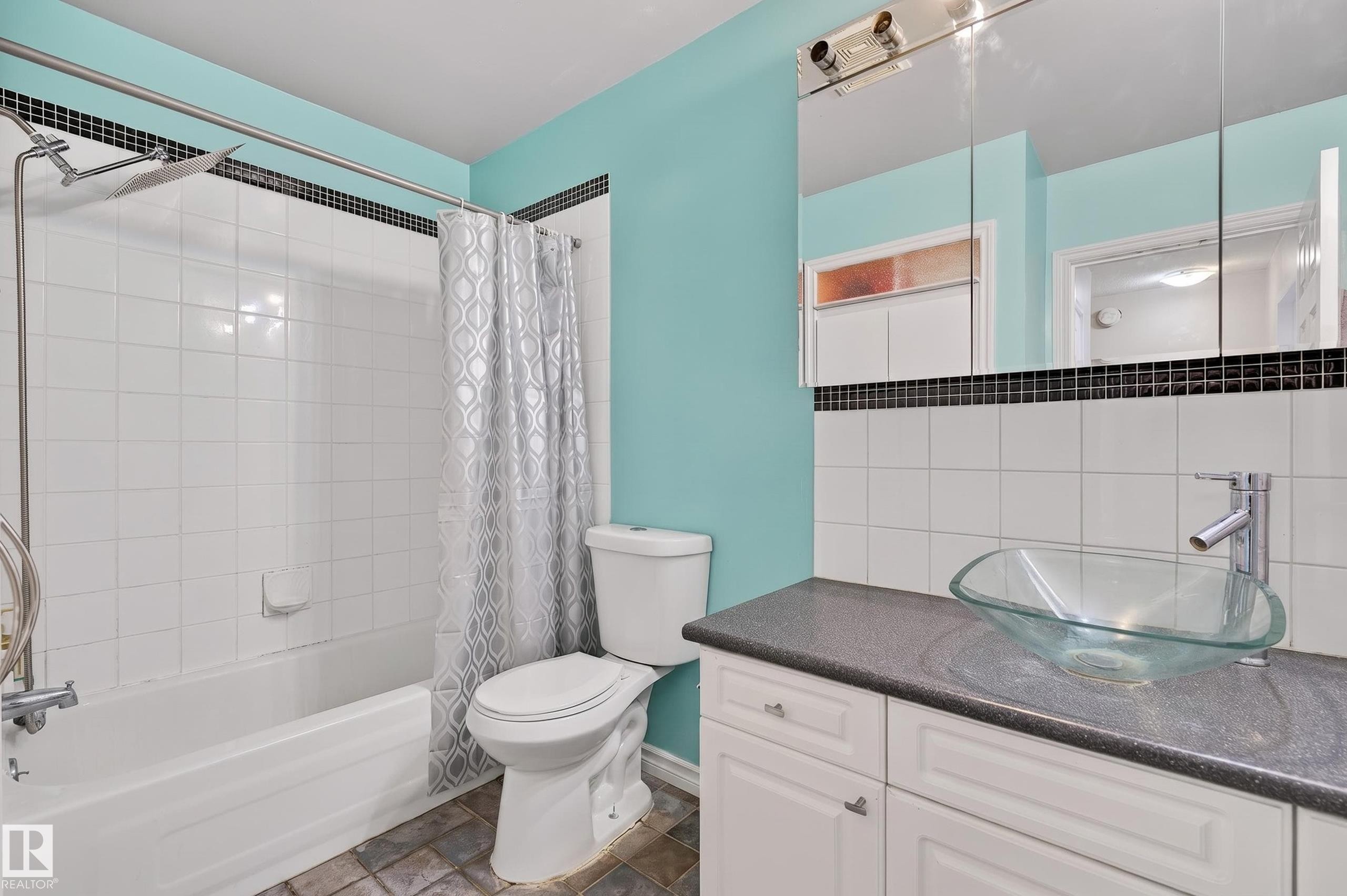 Bathroom featuring a glass vessel sink, dark countertop, and white cabinetry - 26E Meadowlark Village, Edmonton, AB - Indoor Photo Showing Bathroom