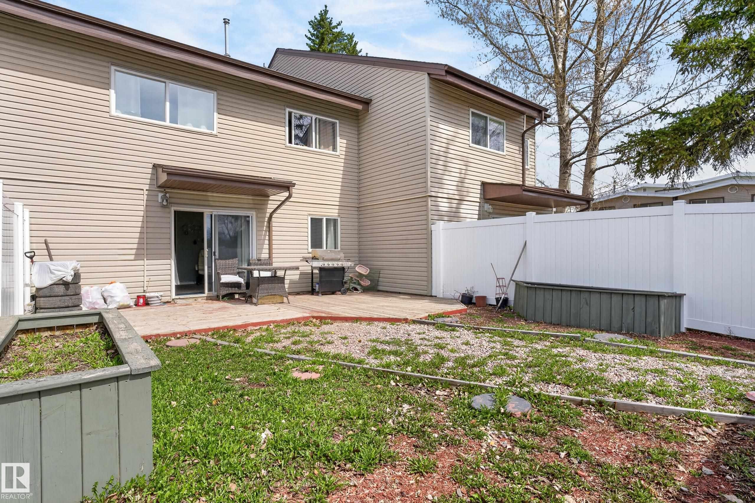 Exterior featuring beige horizontal siding, a private patio area, sliding glass door access, and a white privacy fence - 26E Meadowlark Village, Edmonton, AB - Outdoor With Exterior