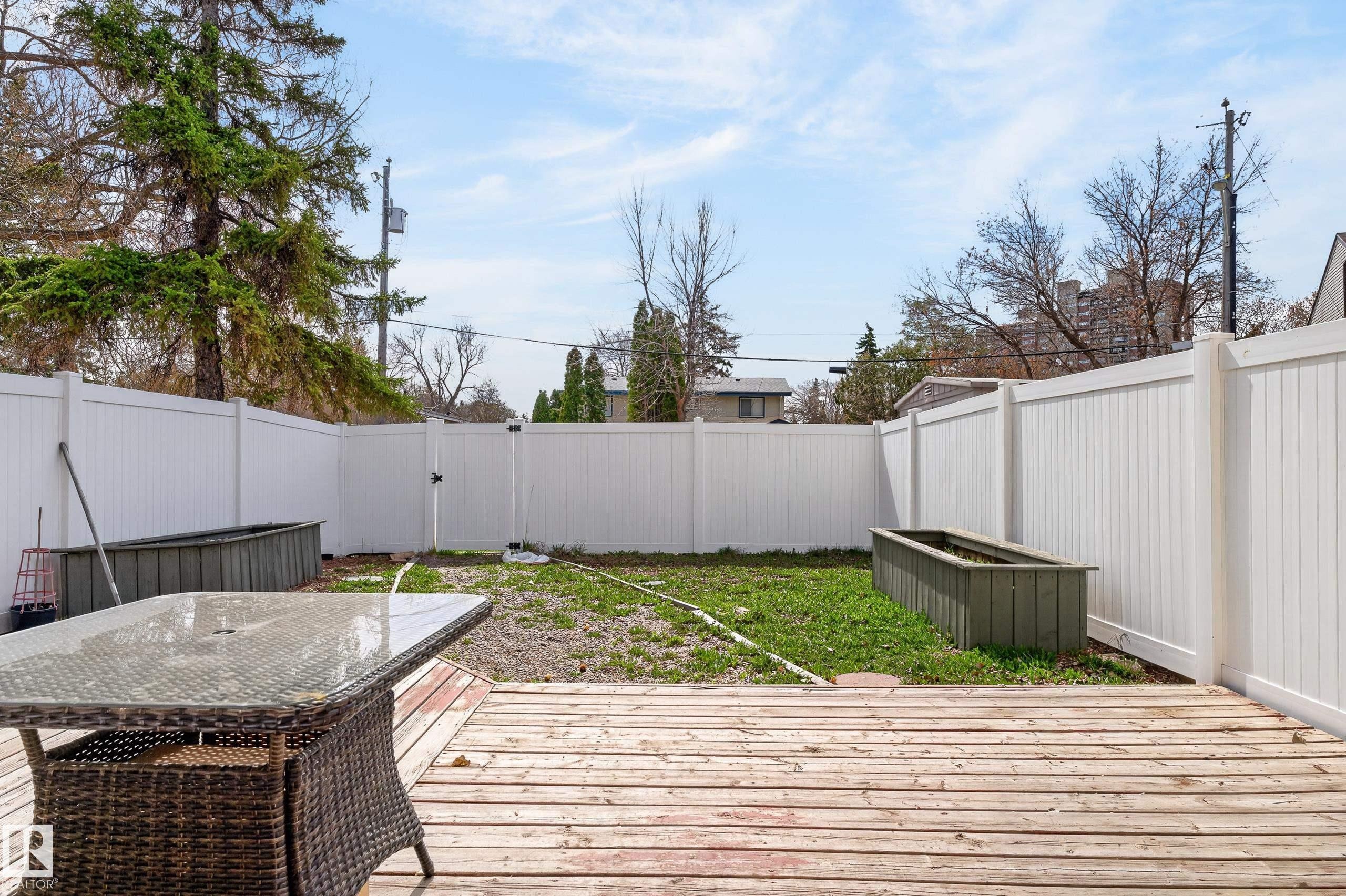 Backyard featuring a wooden deck, white privacy fencing, and two raised garden beds - 26E Meadowlark Village, Edmonton, AB - Outdoor