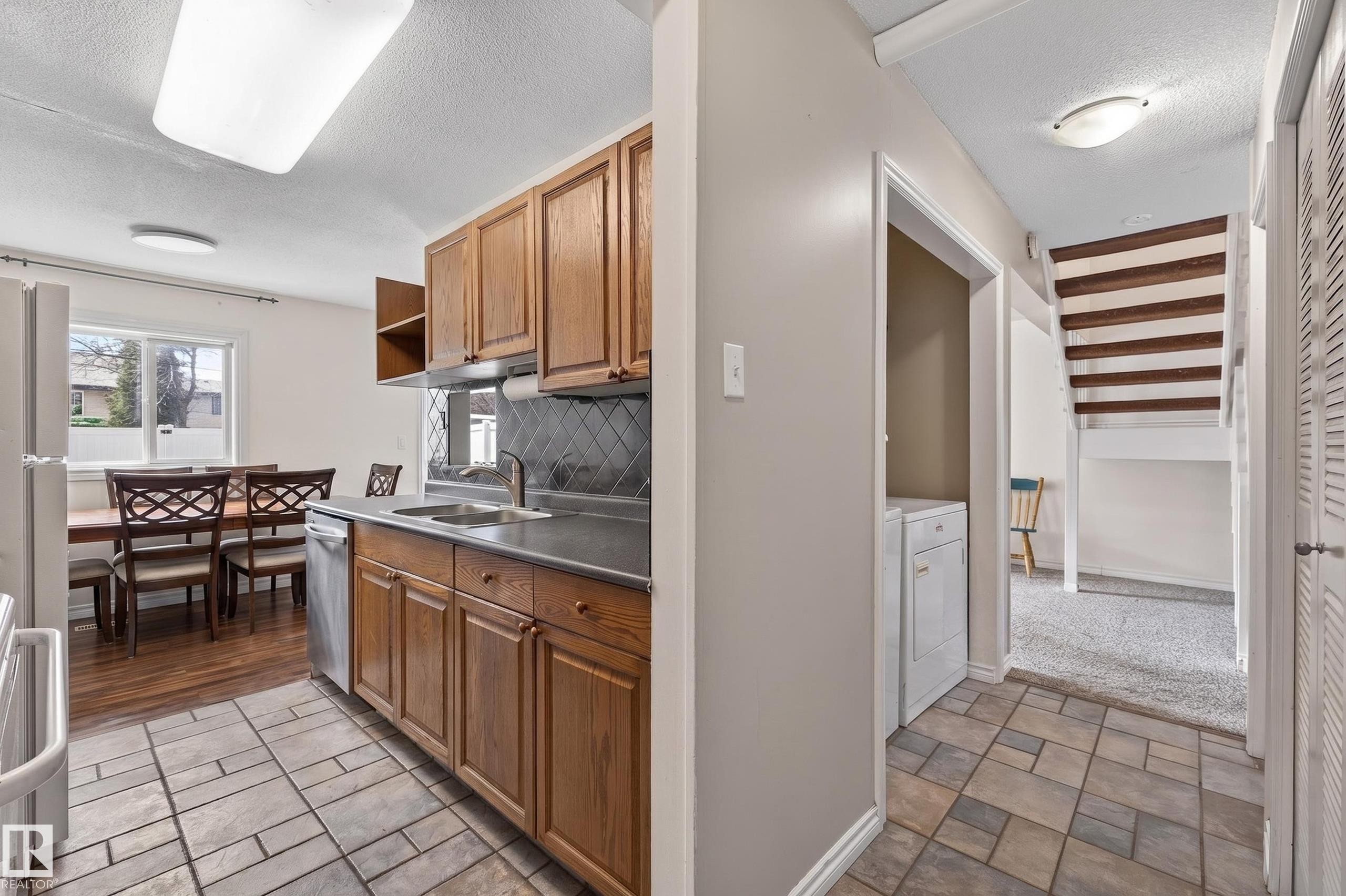 Kitchen featuring wood cabinetry, a stainless steel dishwasher, and a dark countertop with an undermount sink - 26E Meadowlark Village, Edmonton, AB - Indoor Photo Showing Kitchen With Double Sink