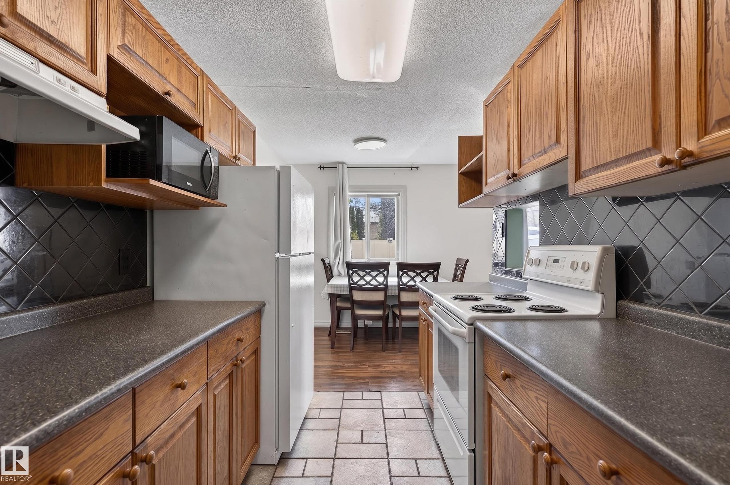 Kitchen featuring wood cabinetry, dark countertops, and a black tile backsplash - 26E Meadowlark Village, Edmonton, AB - Indoor Photo Showing Kitchen