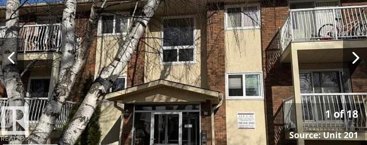 Multi-story residential building exterior featuring brick and stucco facade, individual balconies with white railings, and mature trees - 204 10811 115 Street, Edmonton, AB -