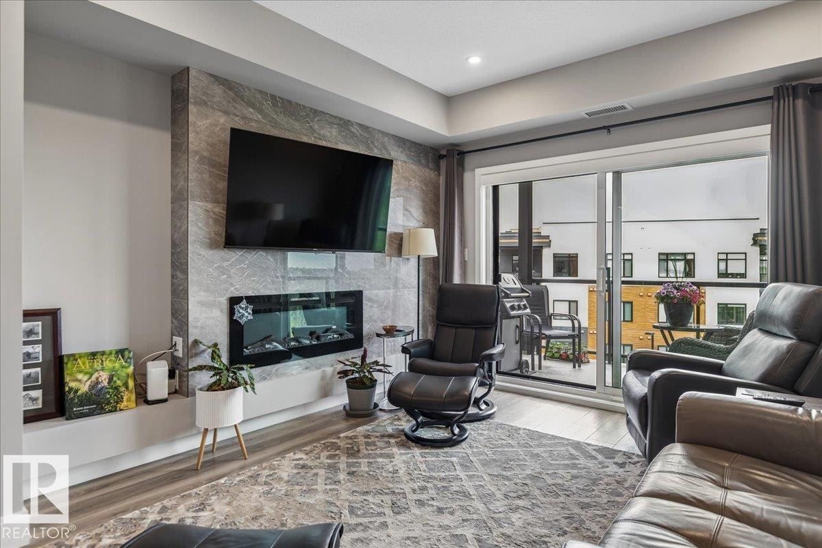 LINEAR ELECTRIC FIREPLACE WITH TILE SURROUND, SLIDING DOOR LEADING TO THE PATIO WITH SOLARIS POWERED SCREEN AND SPECTACULAR RAVINE AND DOWNTOWN VIEWS - 405 7463 May Common, Edmonton, AB - Indoor Photo Showing Living Room With Fireplace