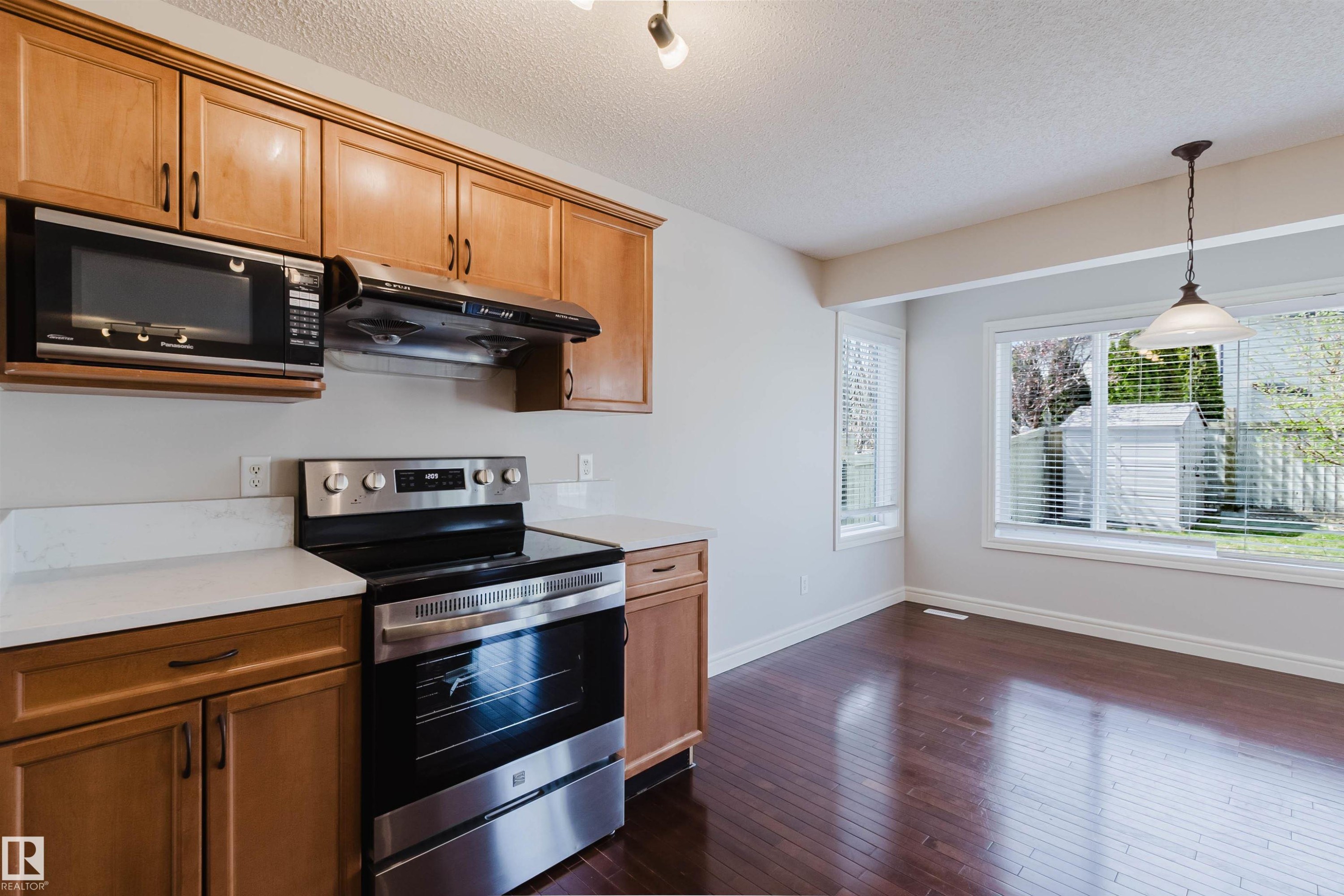 Kitchen and dining area featuring wood-finish flooring, light wood cabinetry, white countertops, and stainless steel appliances - 1140 115 Street, Edmonton, AB - Indoor Photo Showing Kitchen