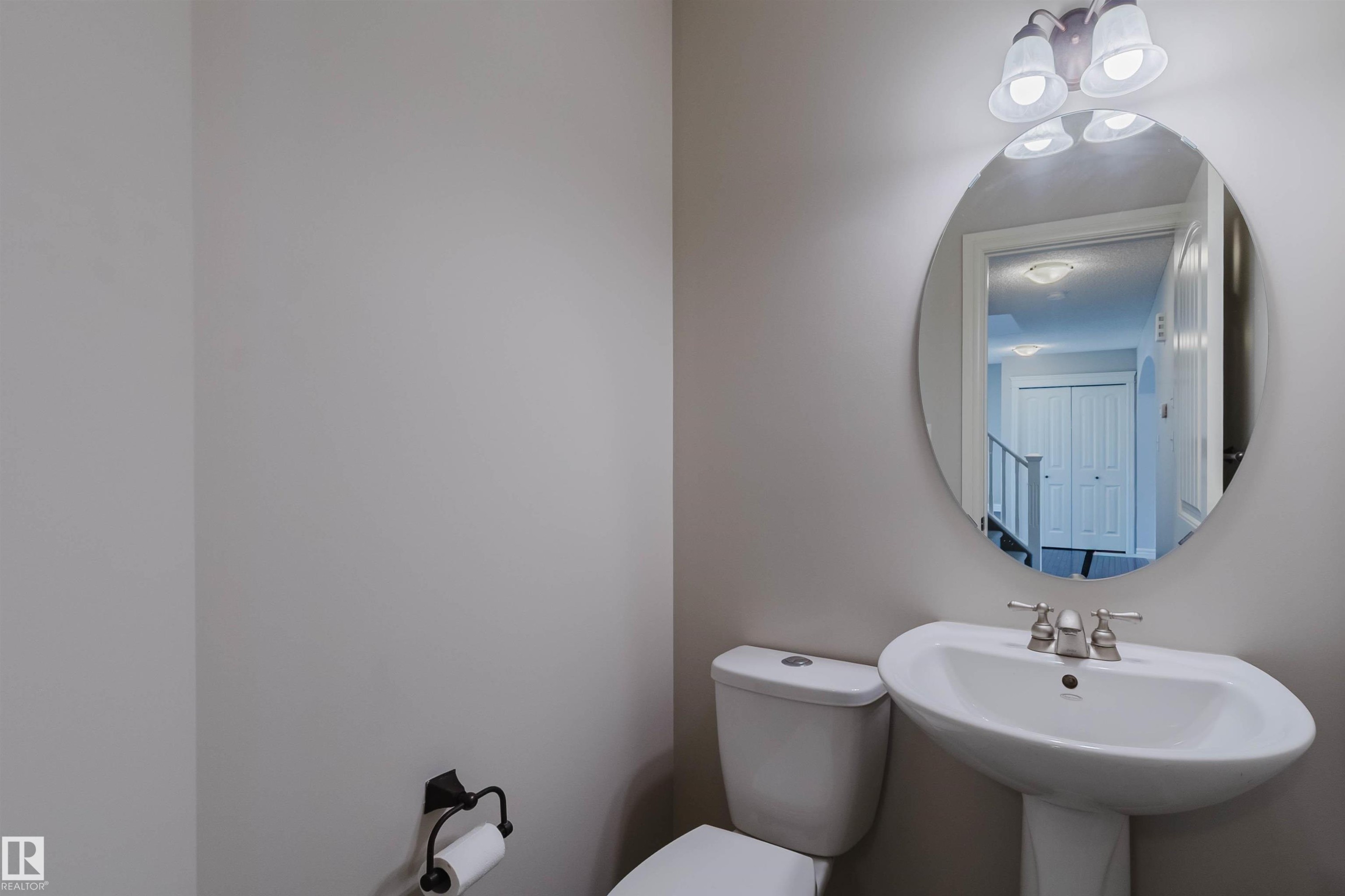 Bathroom featuring an oval mirror, three-light vanity fixture, pedestal sink, and toilet with a wall-mounted toilet paper holder - 1140 115 Street, Edmonton, AB - Indoor Photo Showing Bathroom
