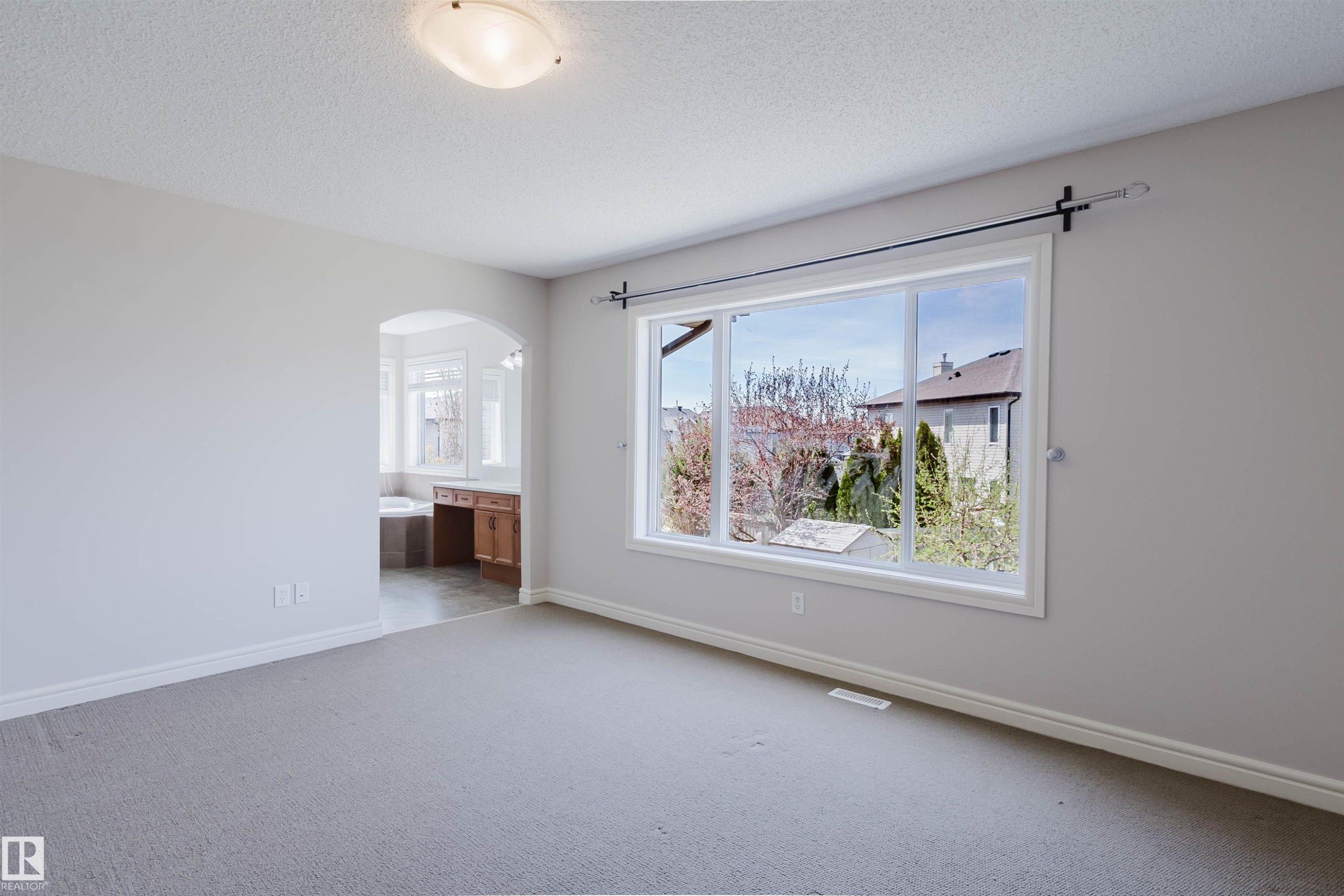 Carpeted room featuring a large window, an arched doorway, and light gray walls - 1140 115 Street, Edmonton, AB - Indoor Photo Showing Other Room