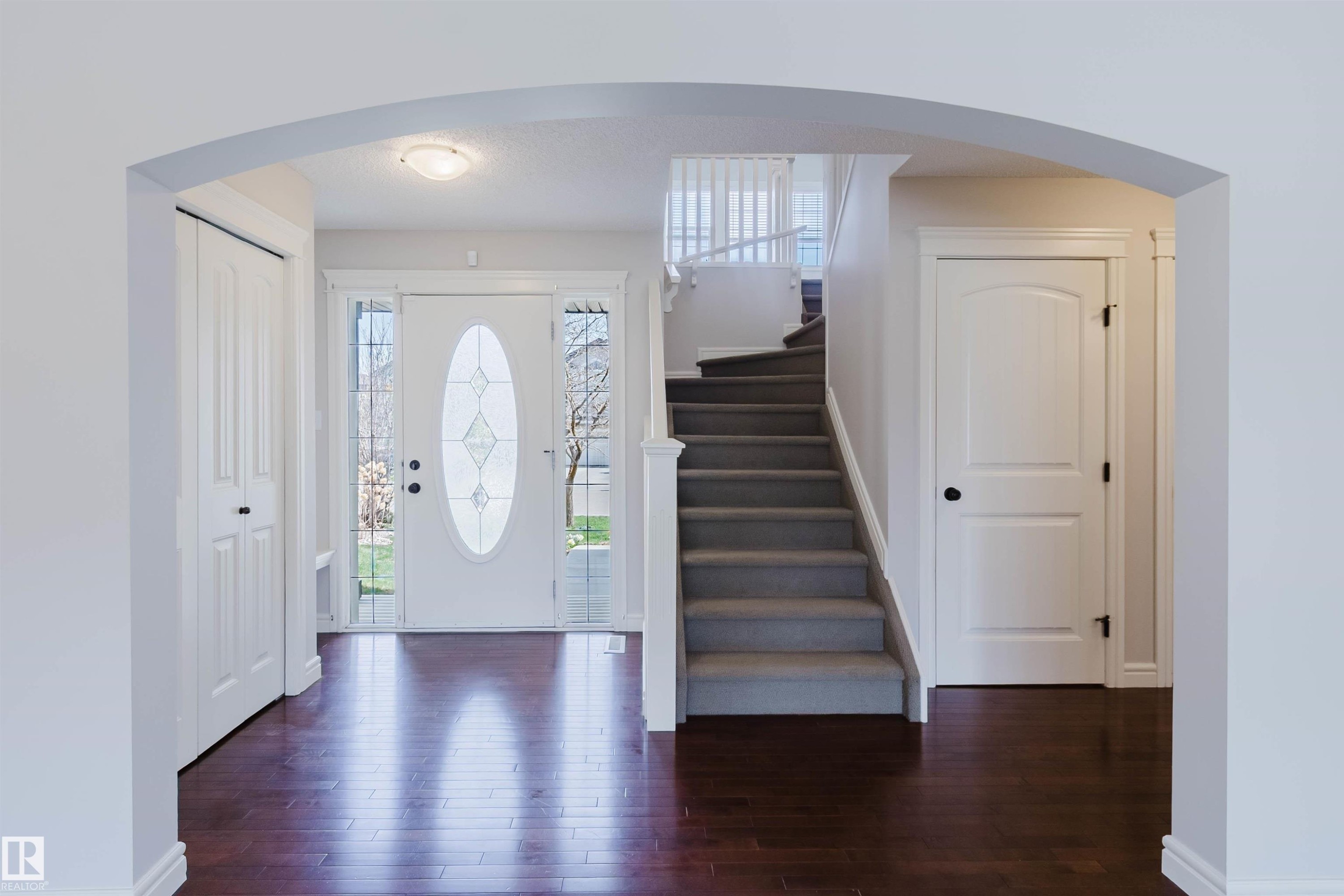 Entryway featuring rich wood-finish flooring, an arched doorway, a white front door with decorative glass inserts, sidelight windows, and a carpeted staircase with white railings - 1140 115 Street, Edmonton, AB - Indoor Photo Showing Other Room
